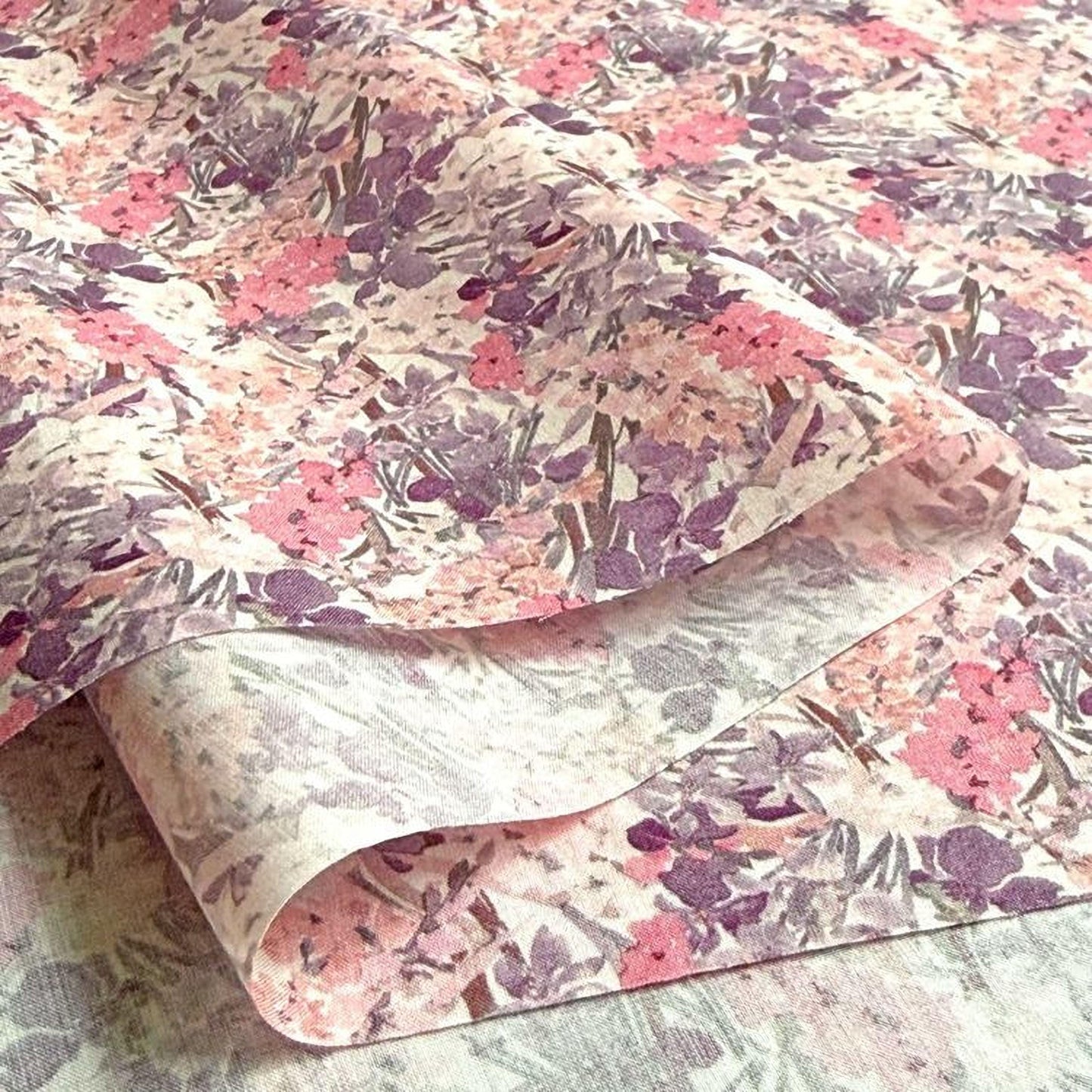 a close-up view of a fabric with a floral pattern in shades of pink and purple. The fabric appears to be folded or rolled, revealing the intricate design of the flowers and leaves.