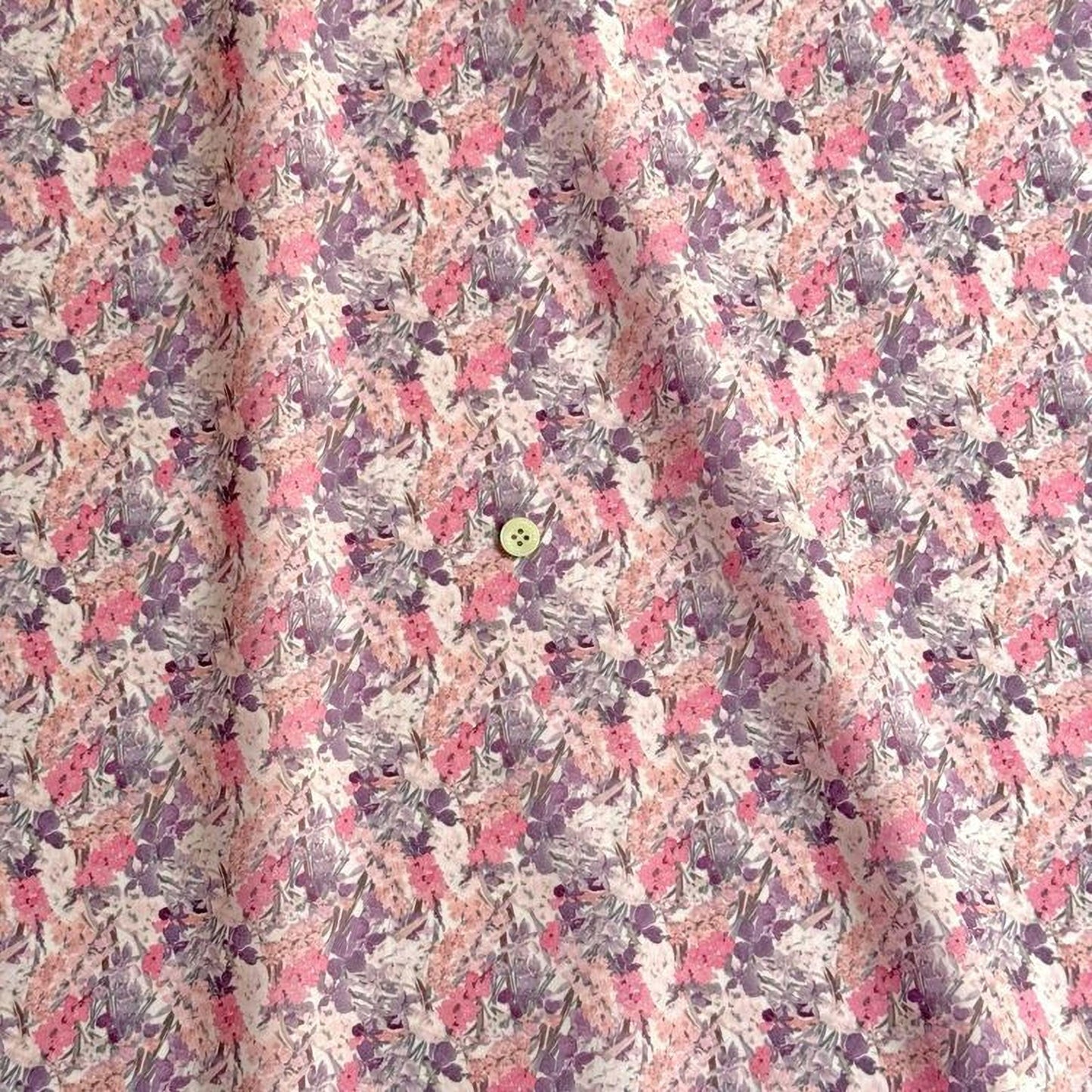 a close-up view of a fabric with a floral pattern in shades of pink and purple. There is a small button visible in the center of the fabric.