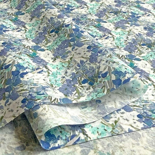 a close-up view of a fabric with a floral pattern in shades of blue and green. The fabric appears to be folded or rolled, revealing the intricate design of the flowers and leaves.