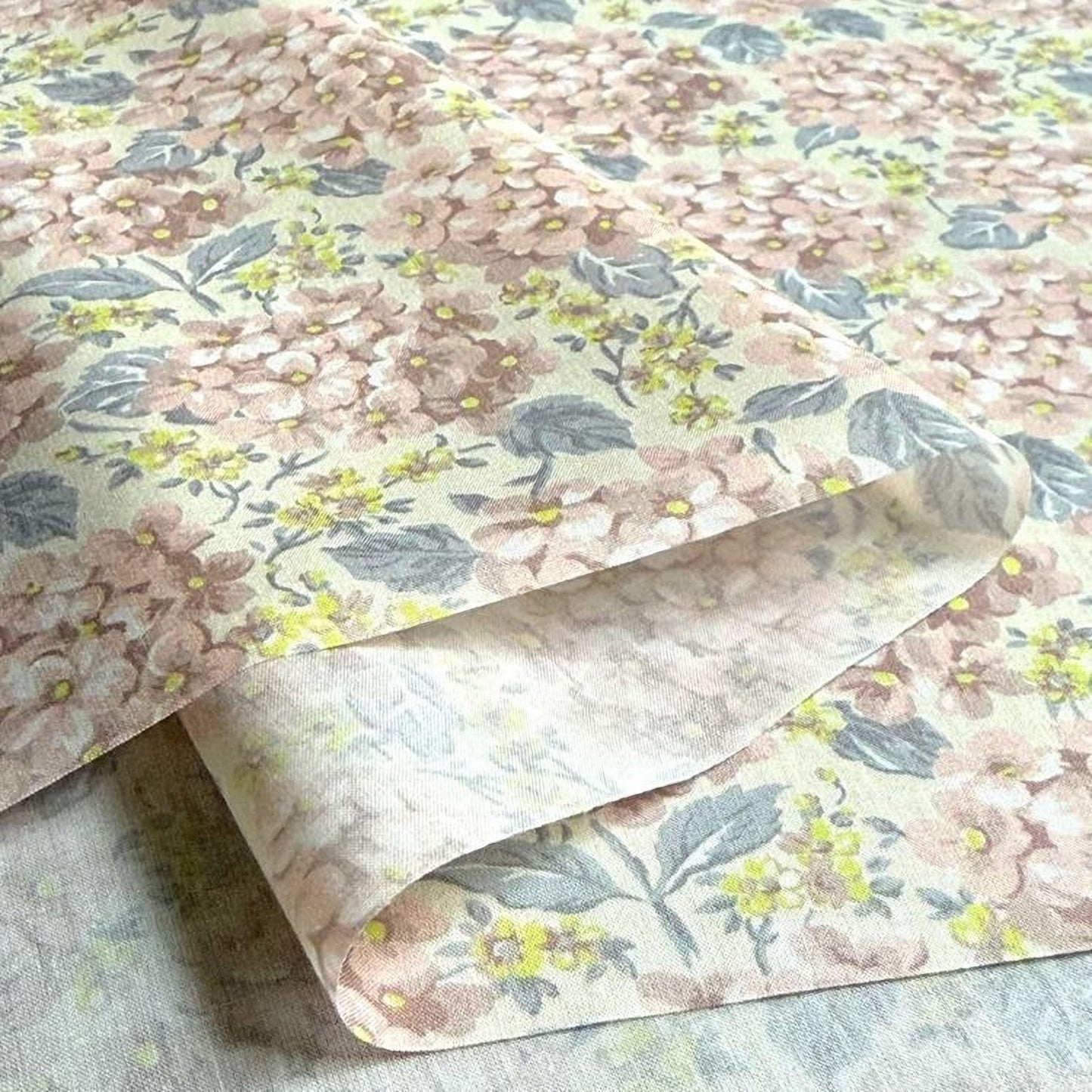 a close-up view of a fabric with a floral pattern, featuring pink and yellow flowers and leaves. The fabric appears to be folded or rolled, revealing the intricate design underneath.