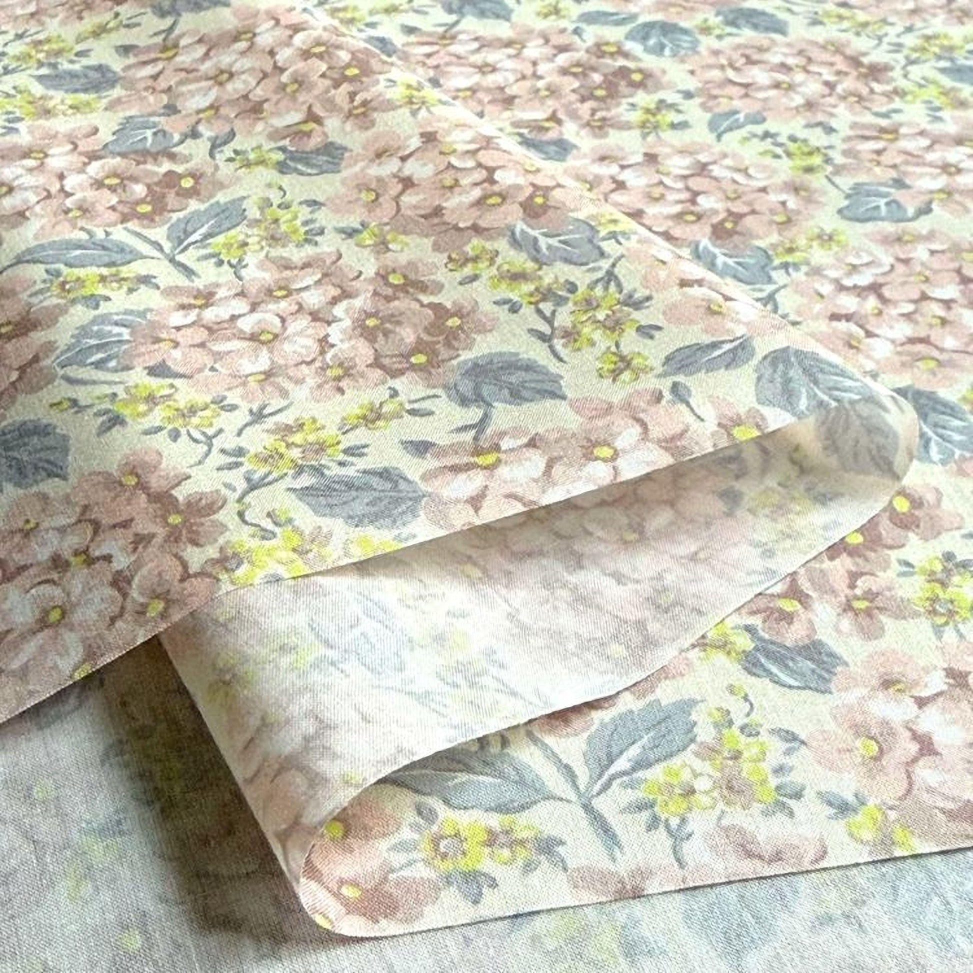 a close-up view of a fabric with a floral pattern, featuring pink and yellow flowers and leaves. The fabric appears to be folded or rolled, revealing the intricate design underneath.