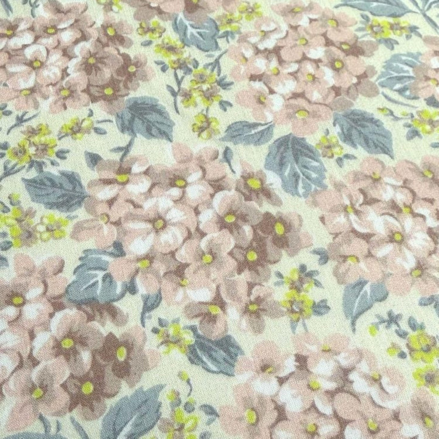 a close-up view of a fabric with a floral pattern. The pattern consists of various shades of pink and yellow flowers, along with green leaves, creating a visually appealing and vibrant design.