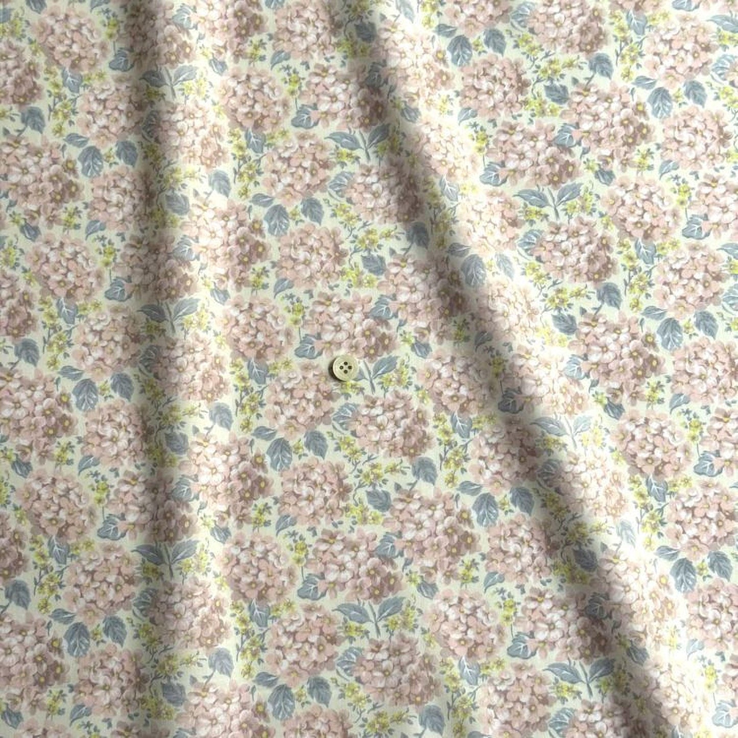 a fabric with a floral pattern, featuring a repeating design of pink and green flowers. There is a small button visible in the center of the fabric.