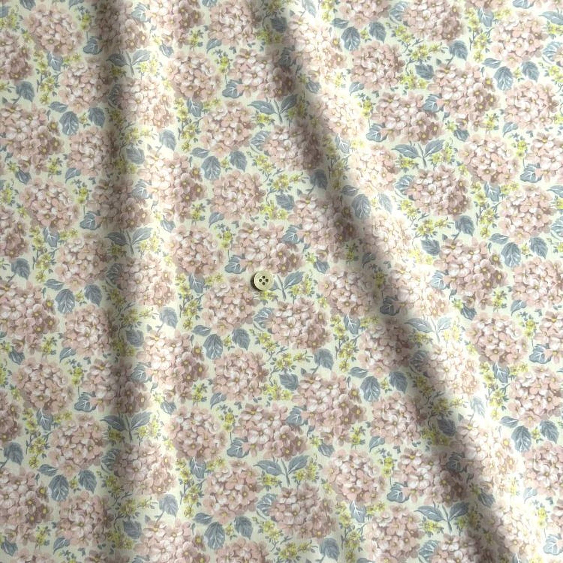 a fabric with a floral pattern, featuring a repeating design of pink and green flowers. There is a small button visible in the center of the fabric.