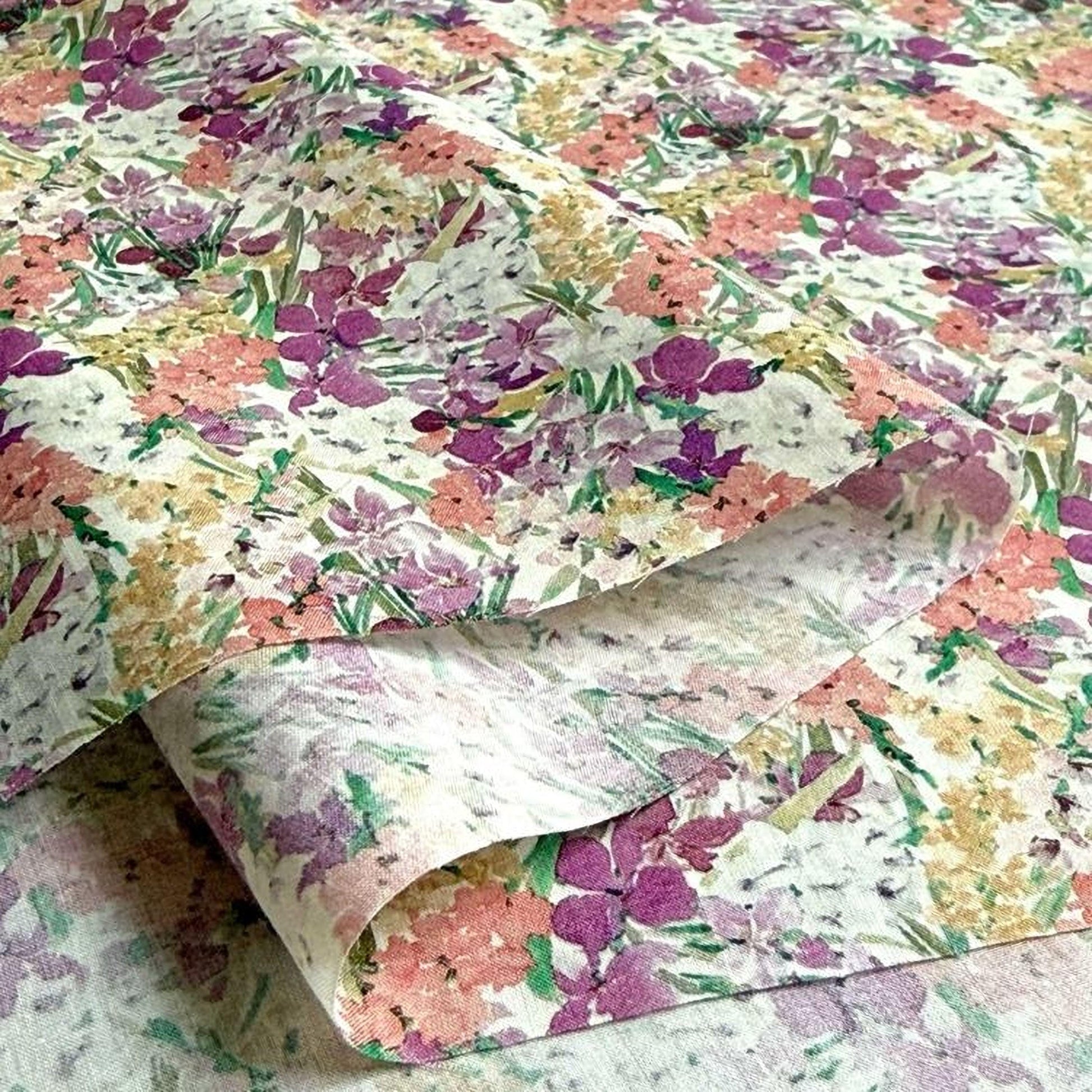 a close-up view of a fabric with a floral pattern, including various shades of purple, pink, and yellow flowers. The fabric appears to be folded or rolled, creating a visually appealing and textured appearance.