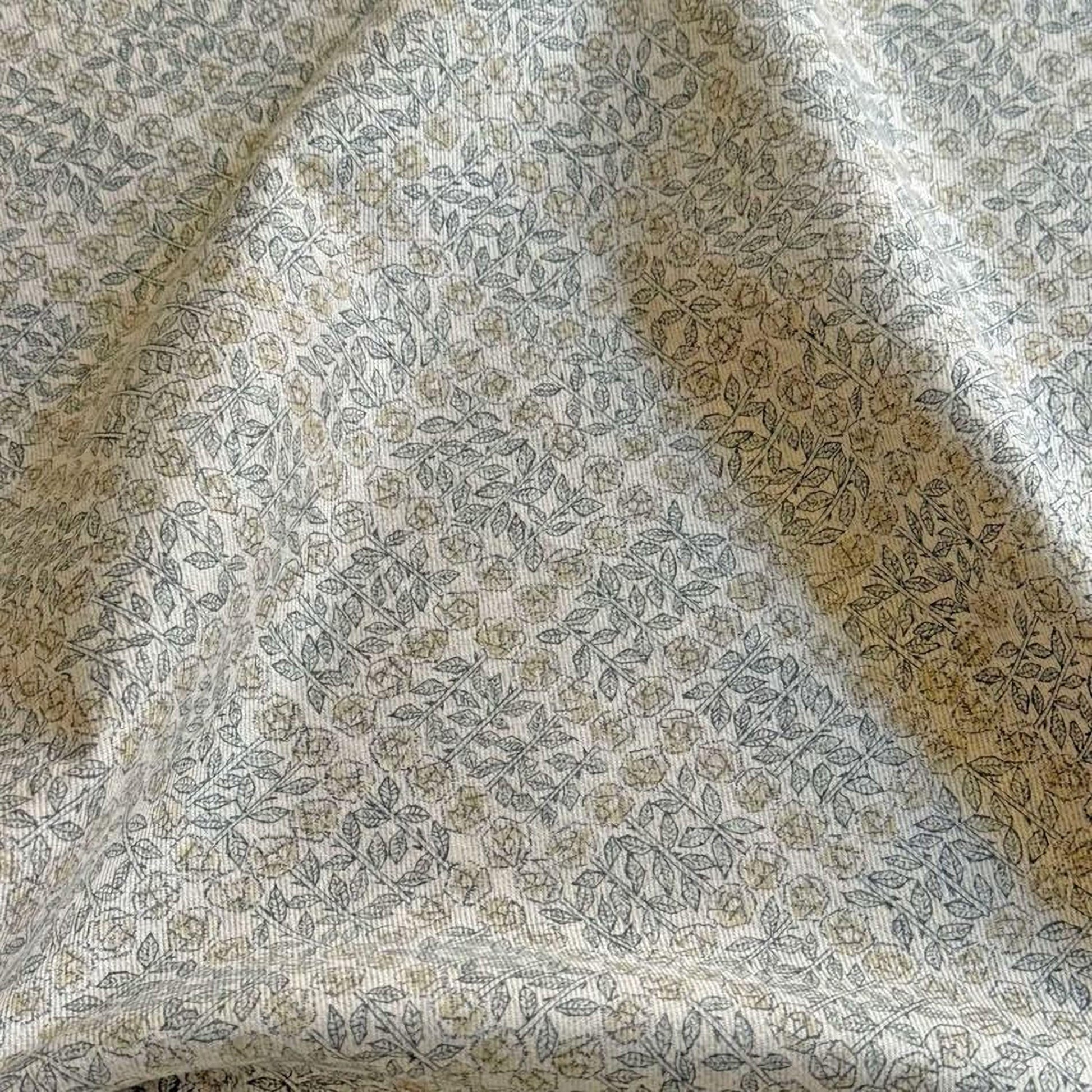 a close-up view of a fabric with a repeating pattern of leaves and flowers in shades of green and gray.