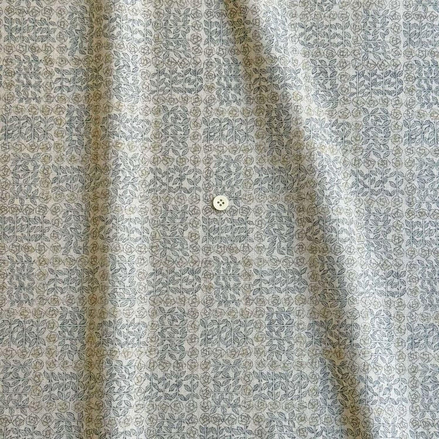 a close-up view of a fabric with a repeating pattern of small flowers or leaves in shades of gray and beige. There is a small white button visible in the center of the fabric.