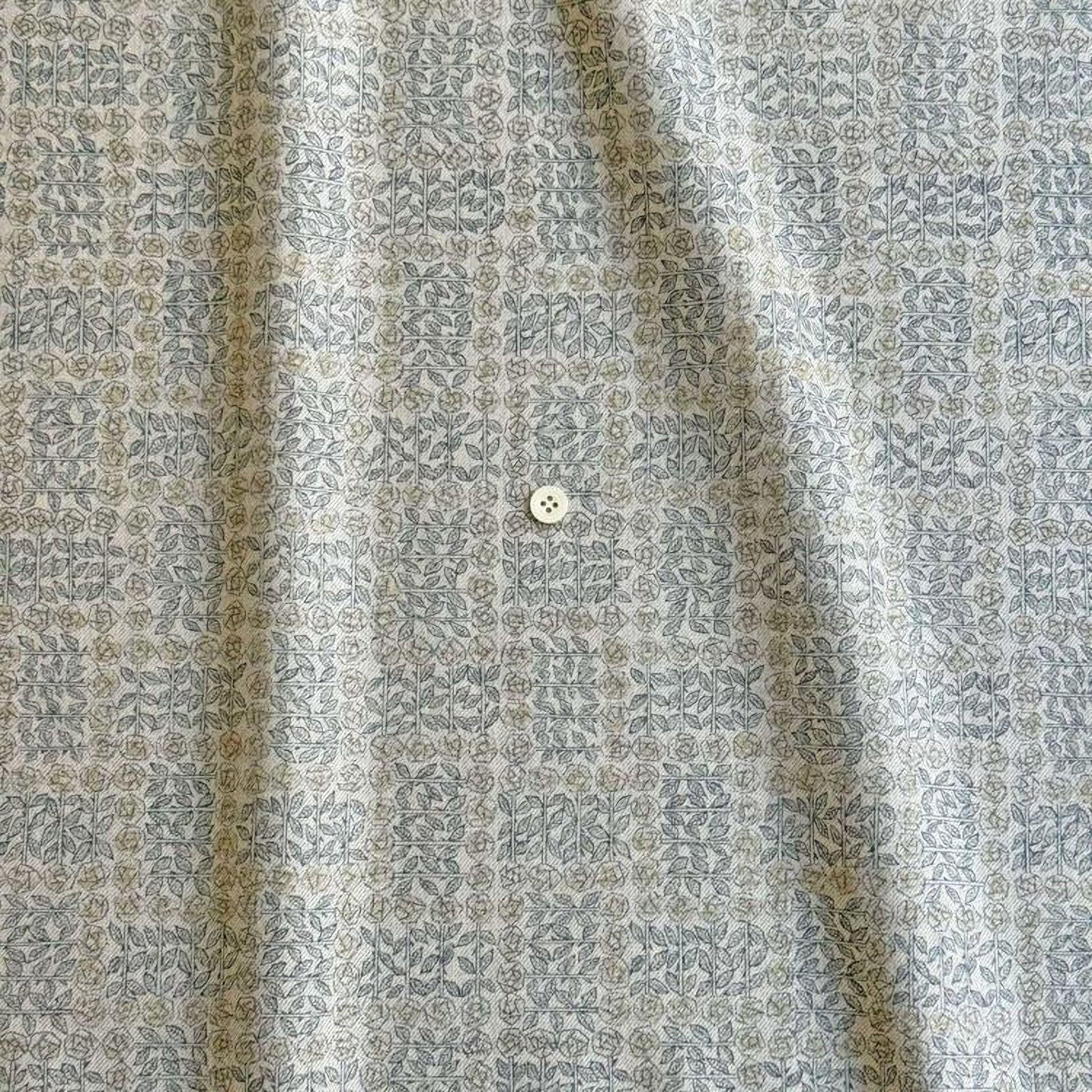 a close-up view of a fabric with a repeating pattern of small flowers or leaves in shades of gray and beige. There is a small white button visible in the center of the fabric.