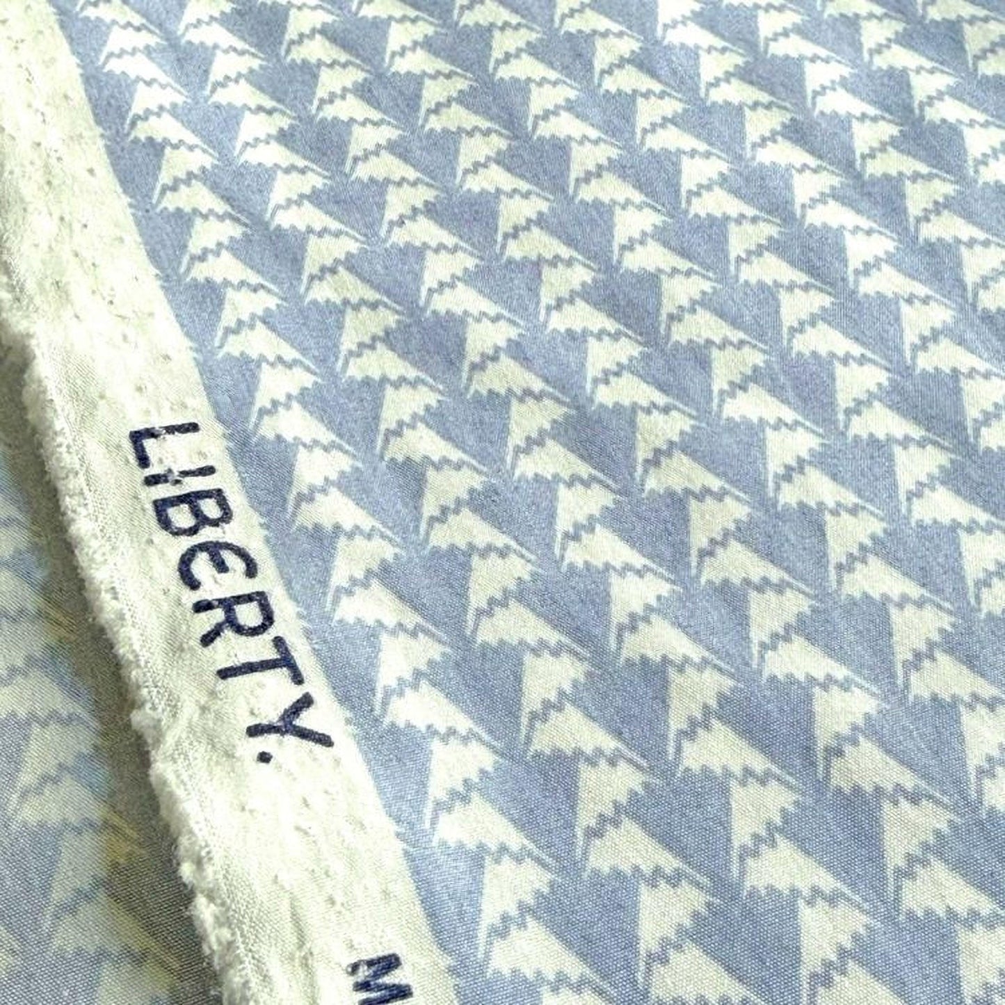 a close-up view of a fabric with a repeating pattern of white triangles on a blue background.