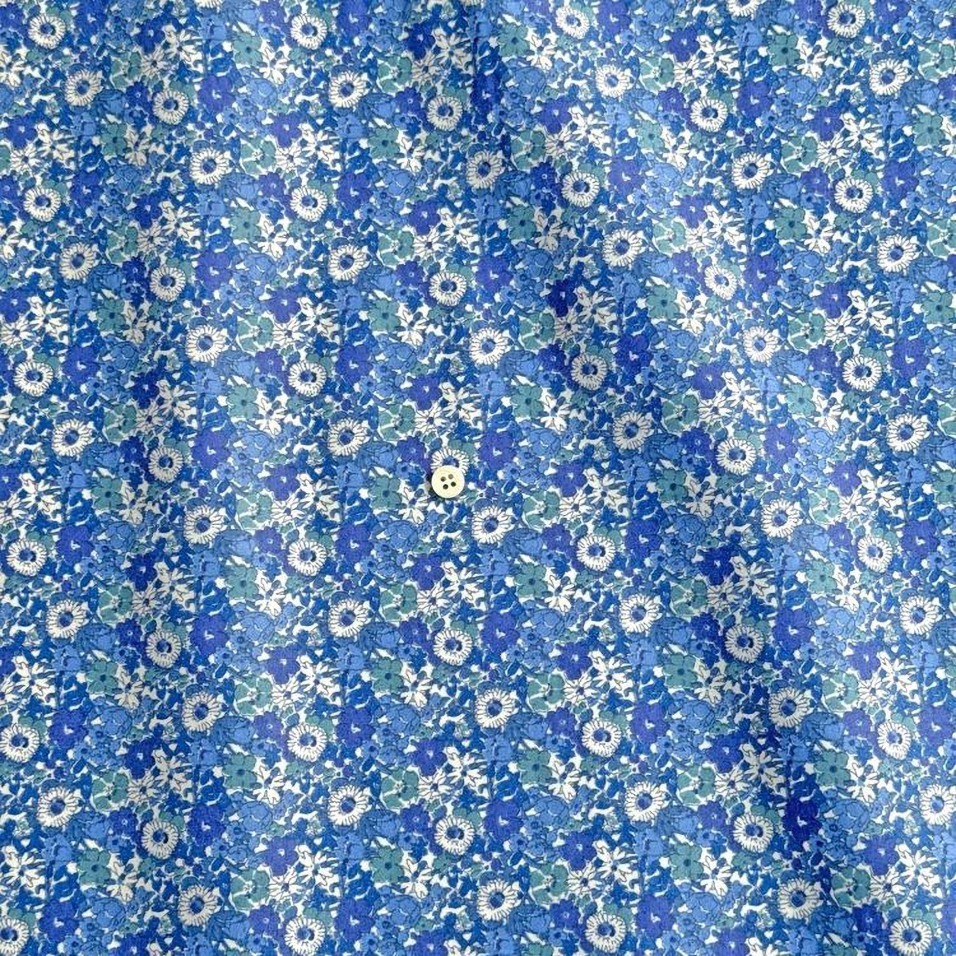 a close-up view of a fabric with a blue and white floral pattern. The fabric appears to be made of a soft, textured material, and there is a small button visible in the center of the pattern.
