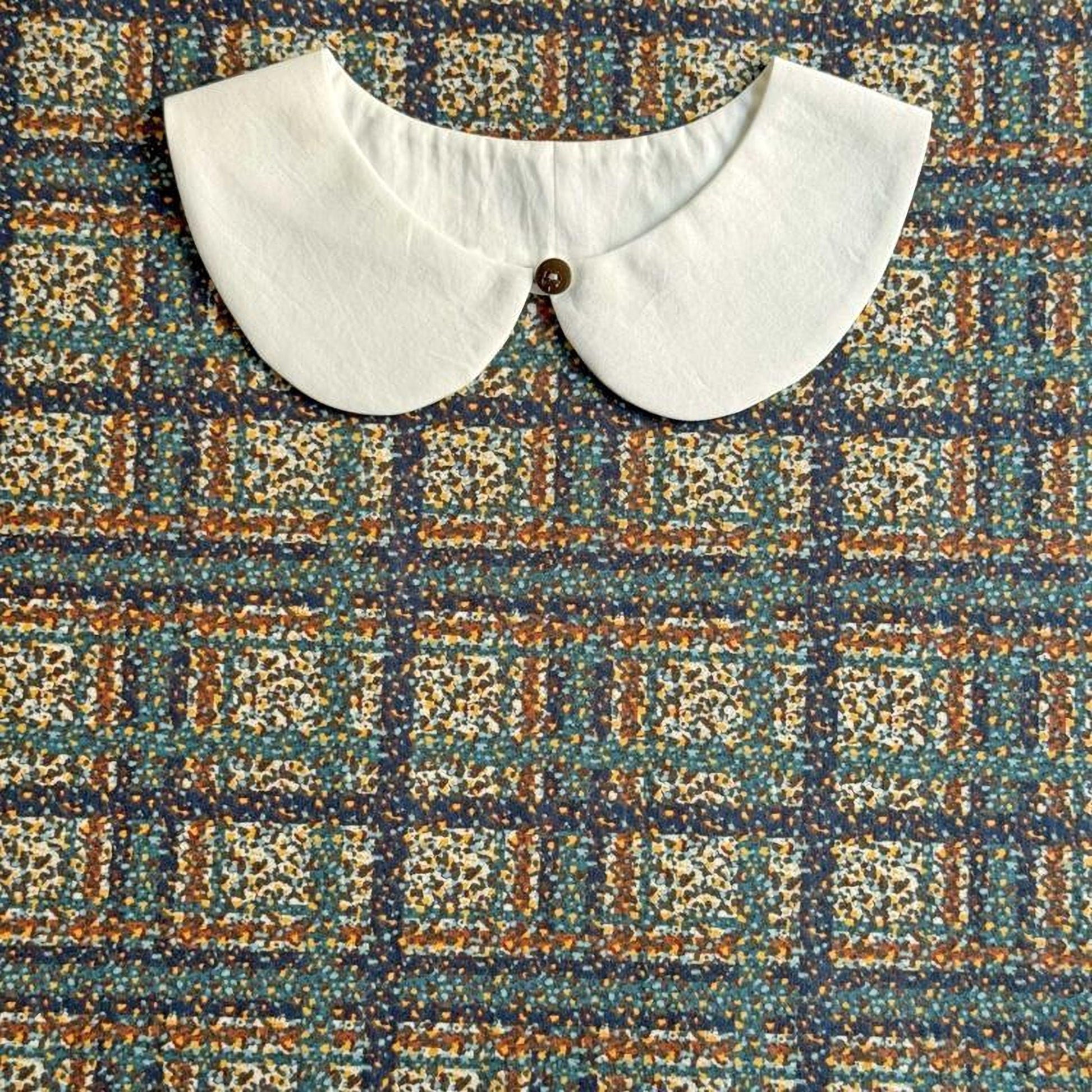 a white collar with a button, placed on a colorful fabric with a geometric pattern.