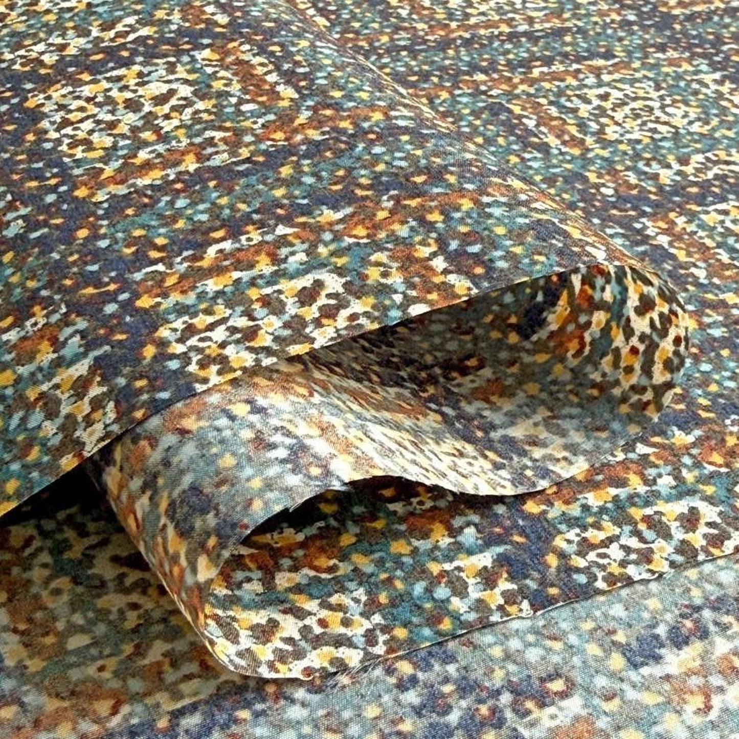 a close-up view of a textured fabric with a colorful, abstract pattern. The fabric appears to be folded or rolled, revealing its intricate design.