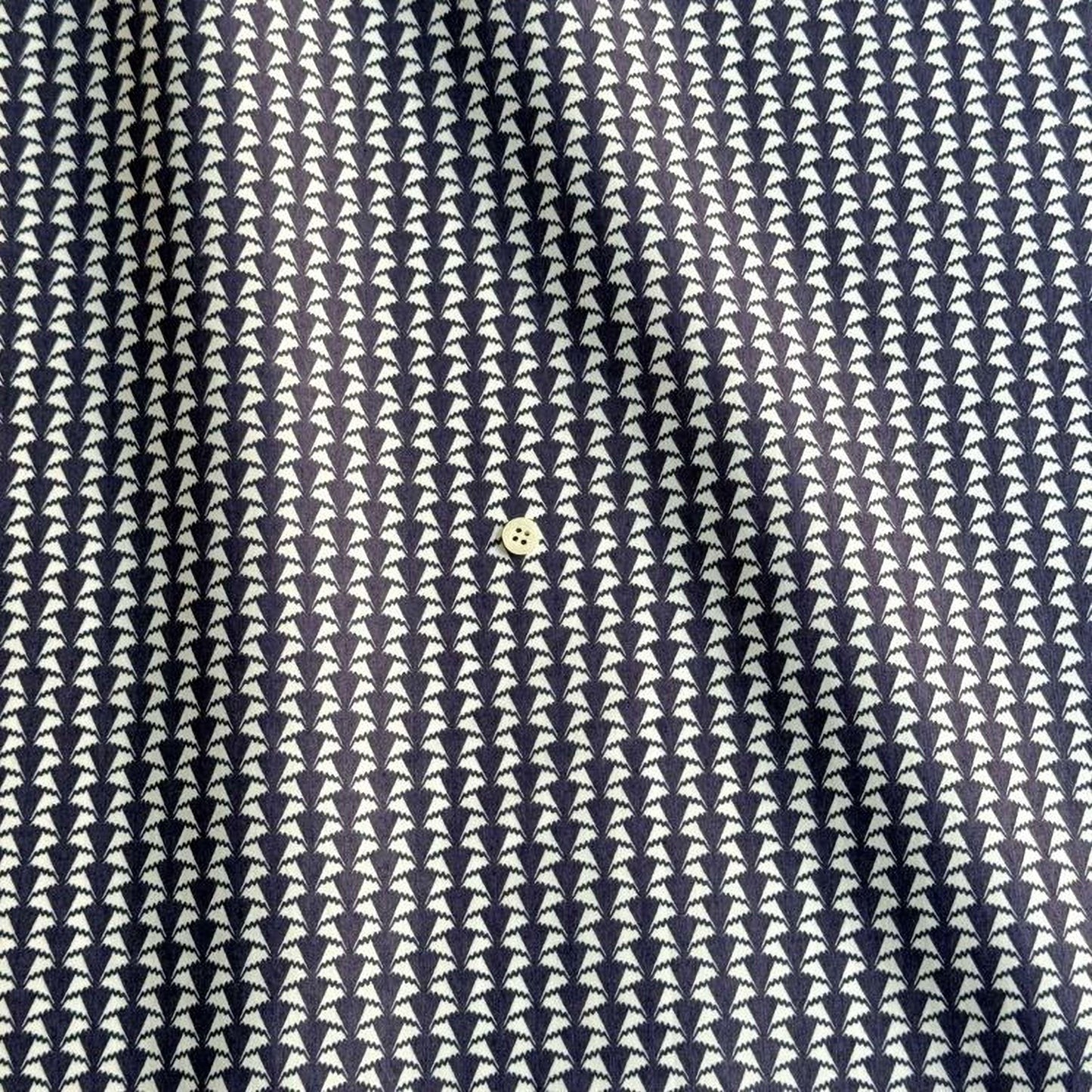 a close-up view of a fabric with a repeating pattern of white triangles arranged in a diagonal grid. The fabric appears to be dark blue, and there is a small white button visible in the center of the pattern.