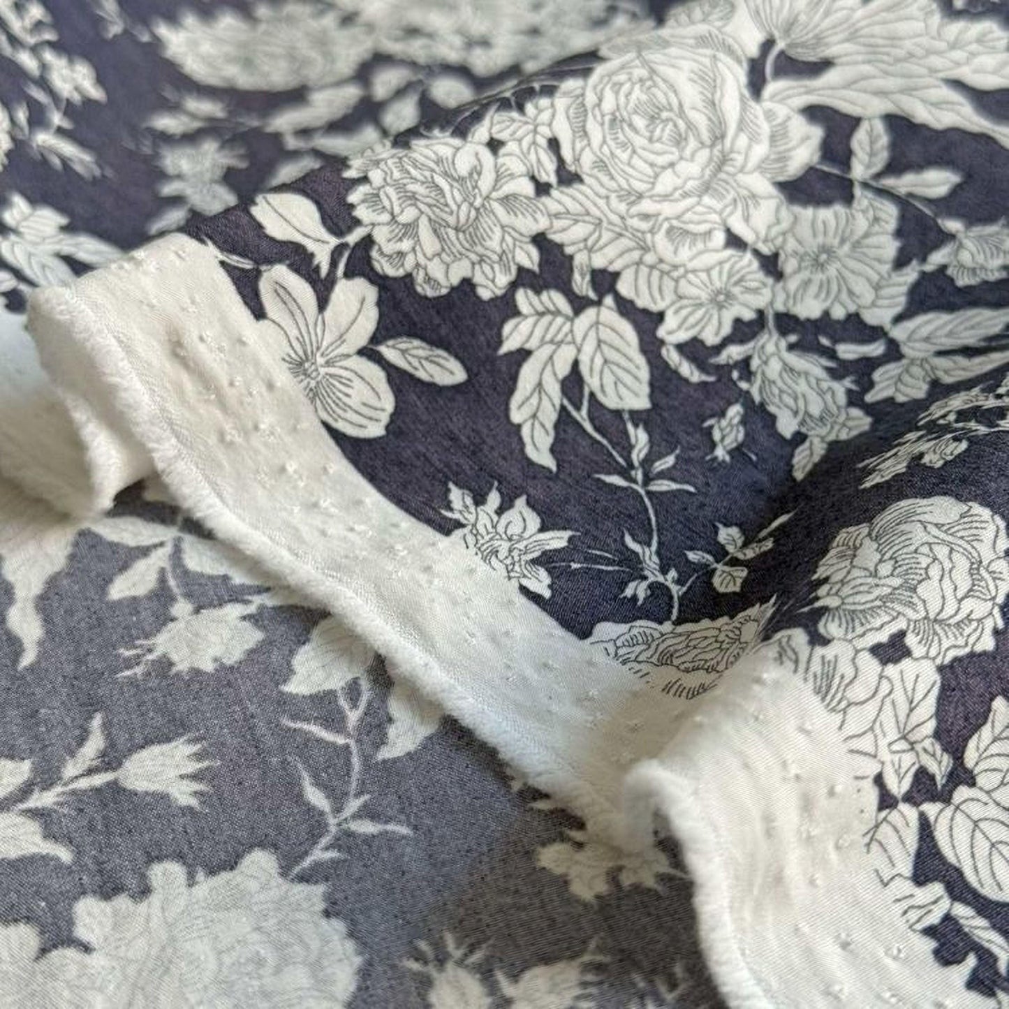a close-up view of a fabric with a floral pattern in shades of blue and white. The fabric appears to be a piece of clothing or textile, with the intricate floral design visible on the surface.