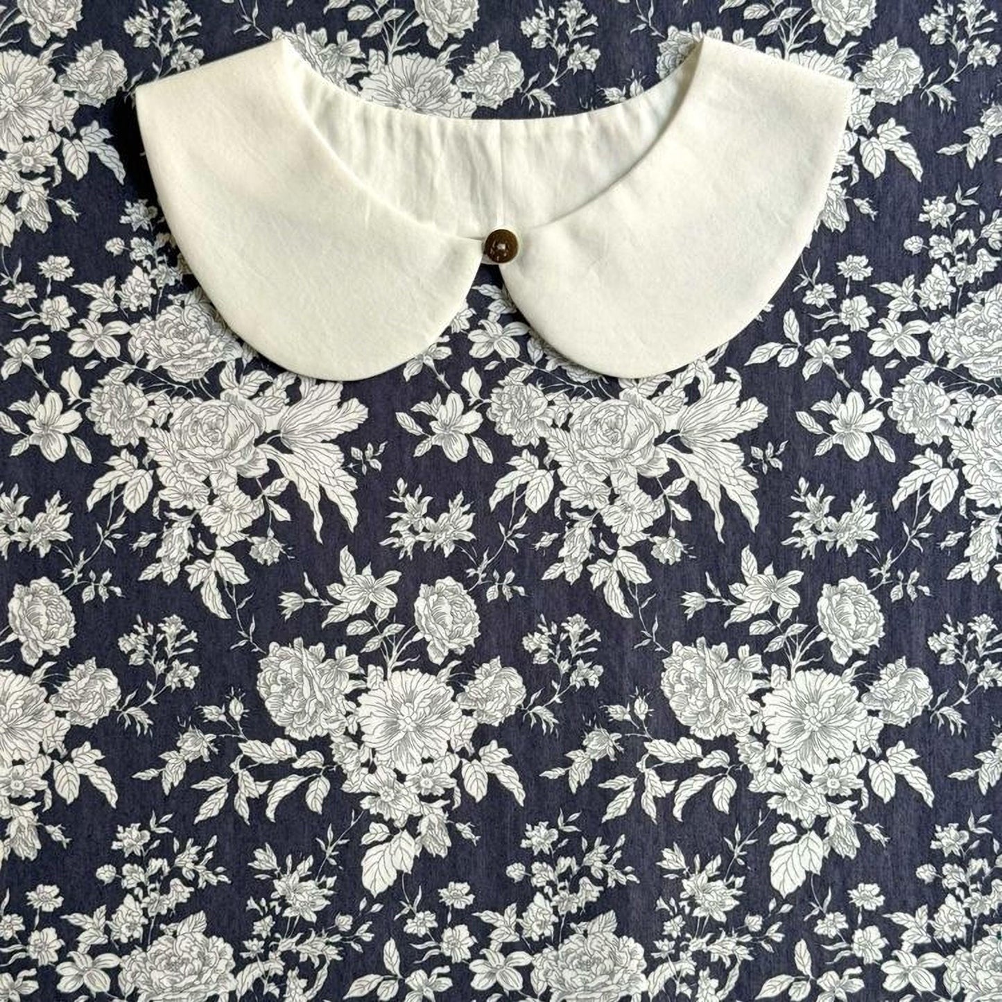 a white collar with a button, set against a dark blue floral background.