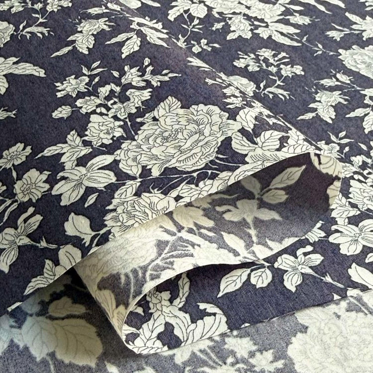 a close-up view of a fabric with a floral pattern in shades of blue and white. The fabric appears to be folded or rolled, revealing the intricate design of the floral pattern.