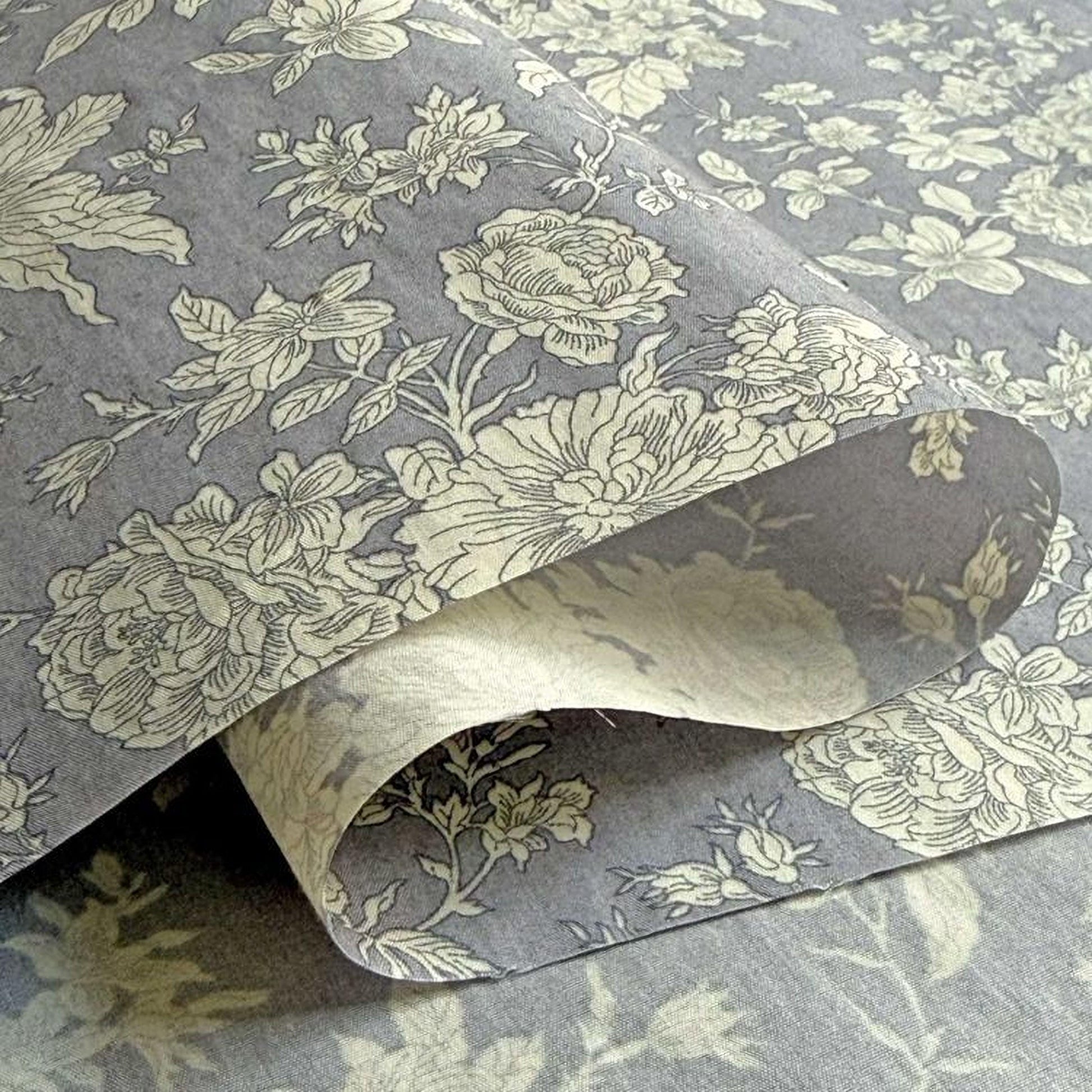a close-up view of a fabric with a floral pattern, including white and gray flowers. The fabric appears to be folded or rolled, revealing the intricate design underneath.