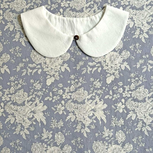 A white collar with a button is displayed against a background of a floral patterned fabric.