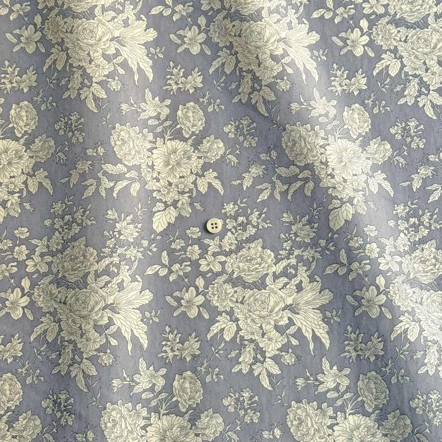 a close-up view of a fabric with a floral pattern in shades of gray and white. The fabric appears to be a piece of clothing, possibly a shirt or blouse, with a button visible in the center.