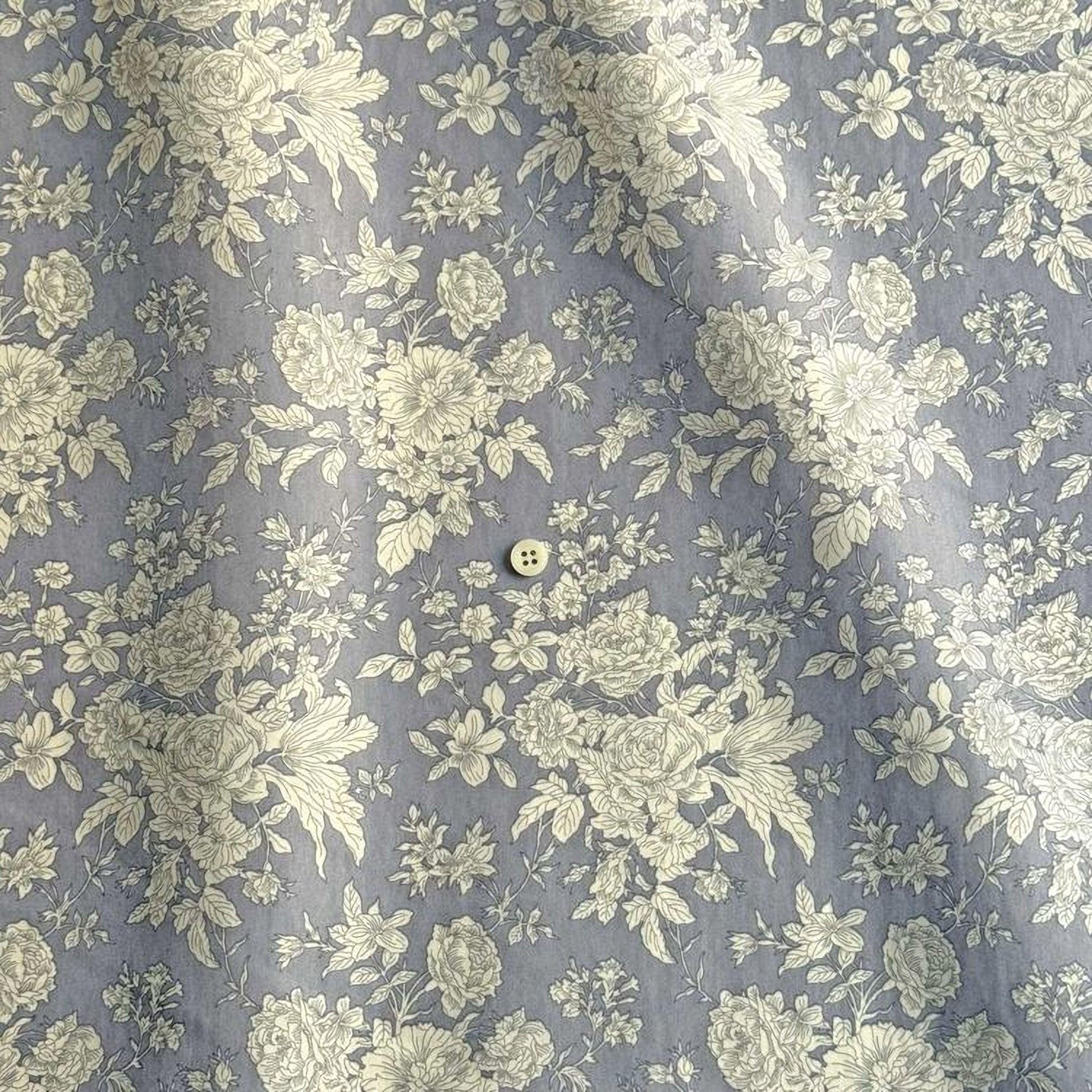 a close-up view of a fabric with a floral pattern in shades of gray and white. The fabric appears to be a piece of clothing, possibly a shirt or blouse, with a button visible in the center.