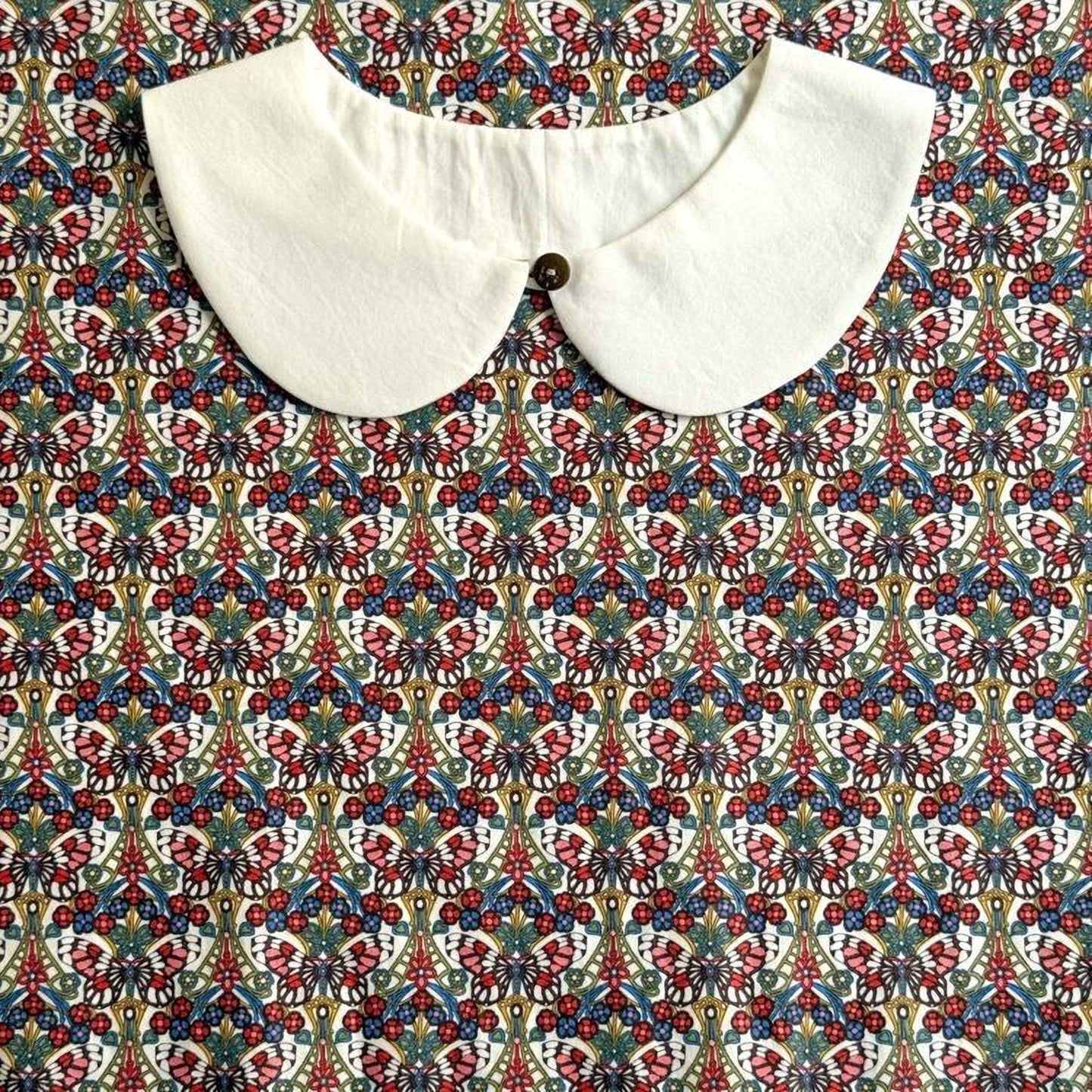 a white collar with a button, set against a colorful, patterned fabric background.