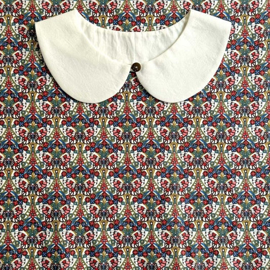 a white collar with a button, set against a colorful, patterned fabric background.