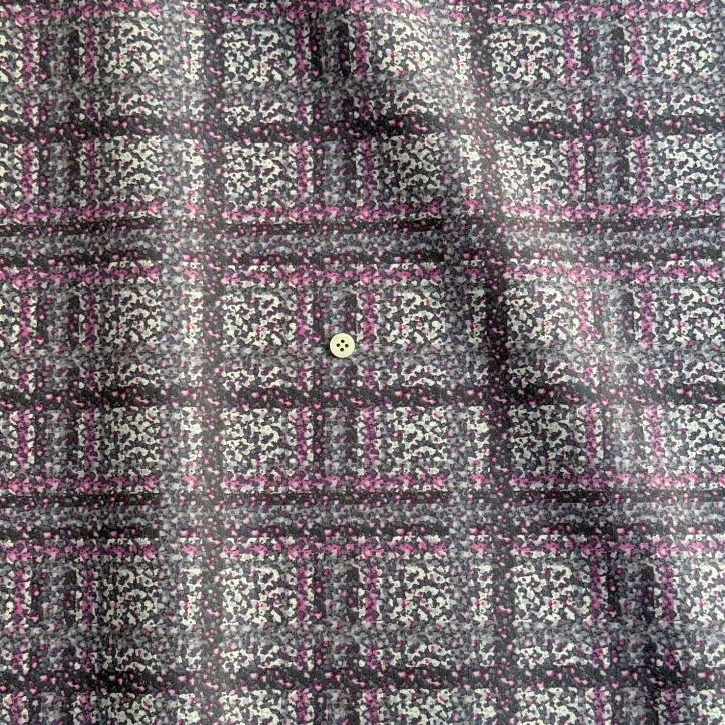 a close-up view of a fabric with a pattern of small squares in shades of pink and gray, creating a checkered or plaid design. There is a small button visible in the center of the pattern.