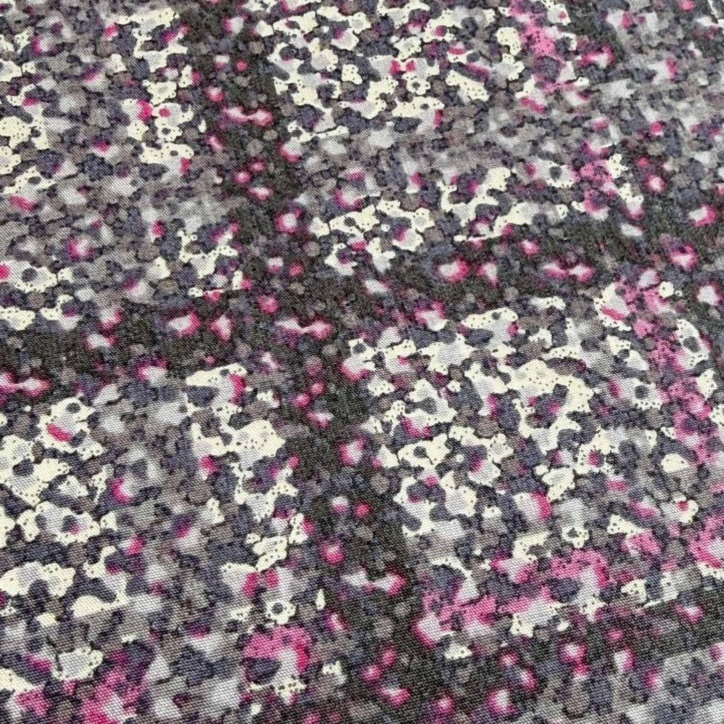The image is a close-up of a fabric with a pattern of small, irregularly shaped dots in shades of pink, gray, and black. The dots are scattered across the fabric, creating a visually striking and textured appearance.