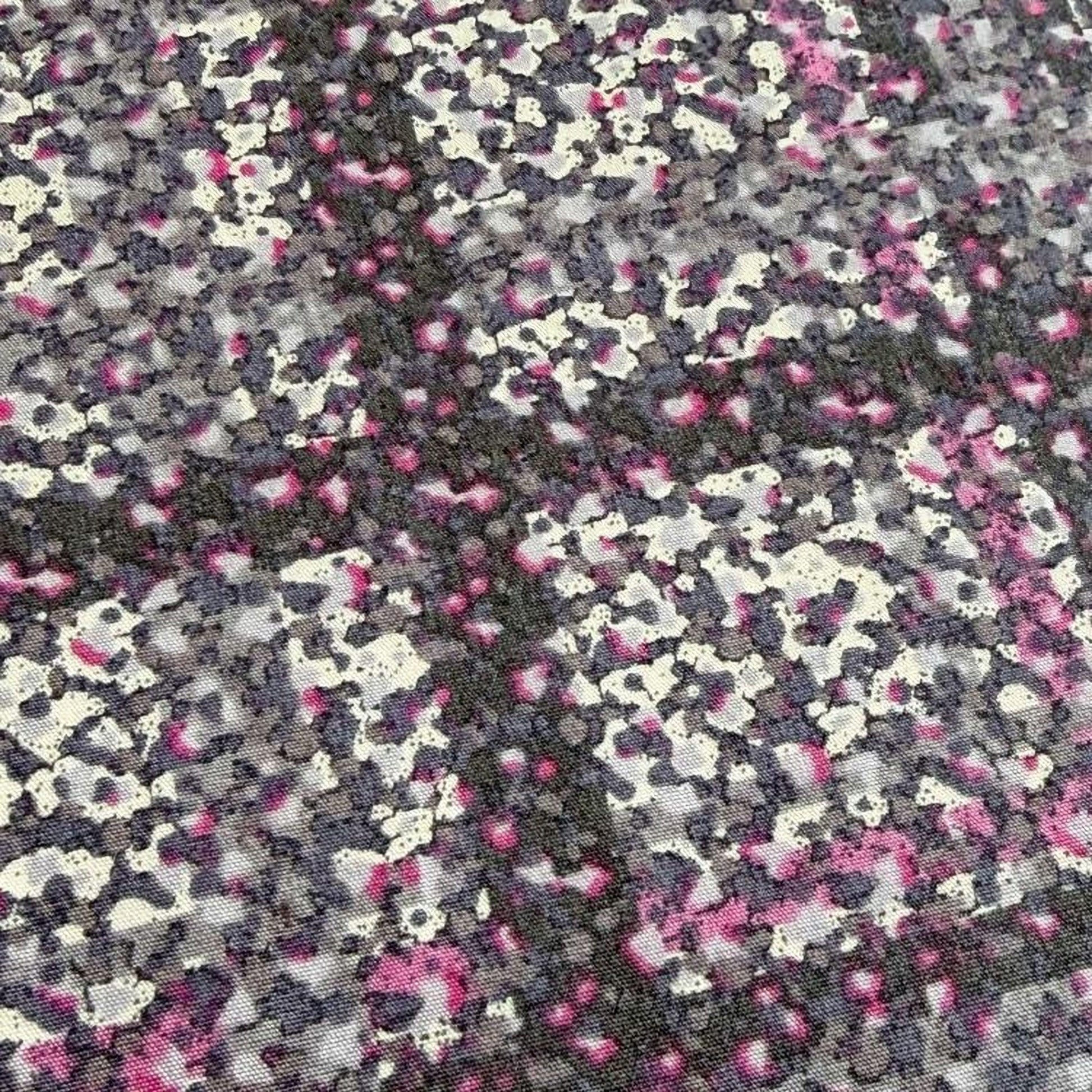 The image is a close-up of a fabric with a pattern of small, irregularly shaped dots in shades of pink, gray, and black. The dots are scattered across the fabric, creating a visually striking and textured appearance.