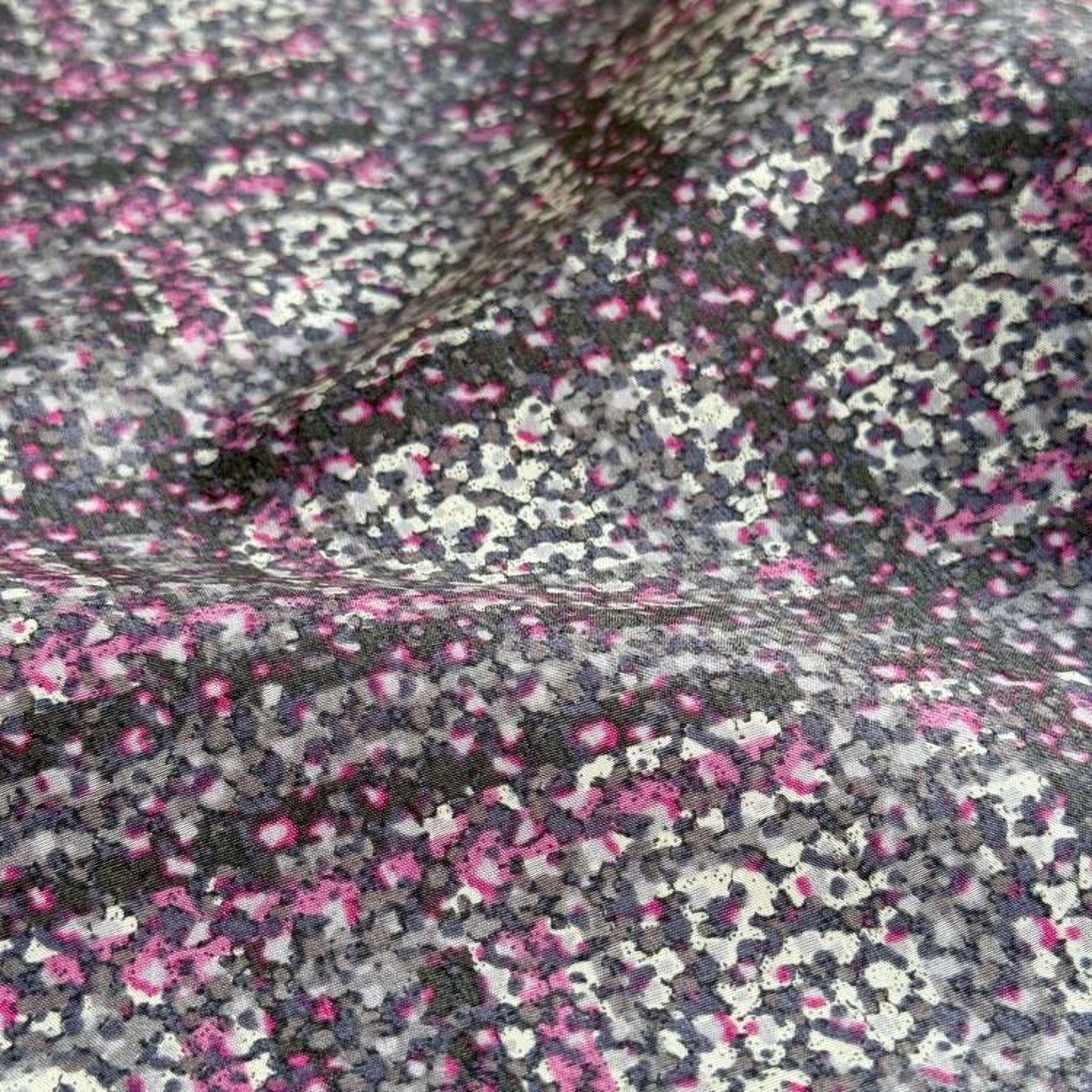 a close-up view of a fabric with a pattern of small, irregularly shaped dots in shades of pink, gray, and black.