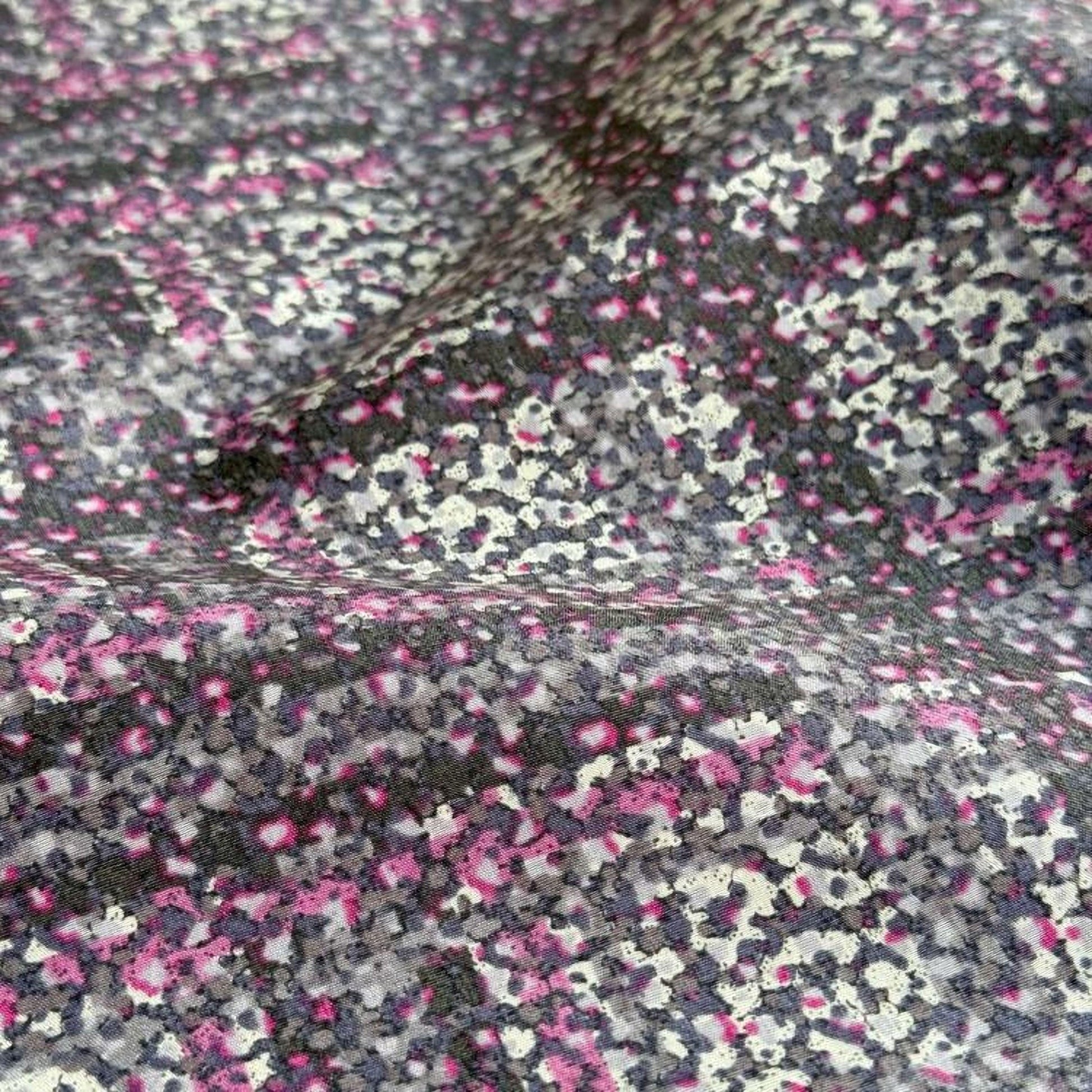 a close-up view of a fabric with a pattern of small, irregularly shaped dots in shades of pink, gray, and black.