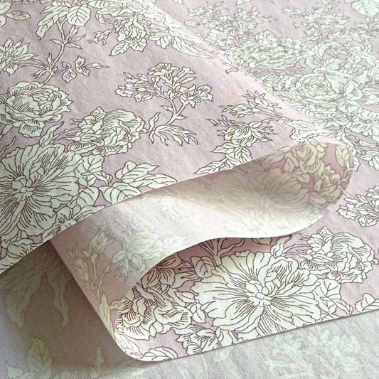 a close-up view of a fabric with a floral pattern in shades of pink and white. The fabric appears to be folded or rolled, revealing the intricate design of the flowers and leaves.