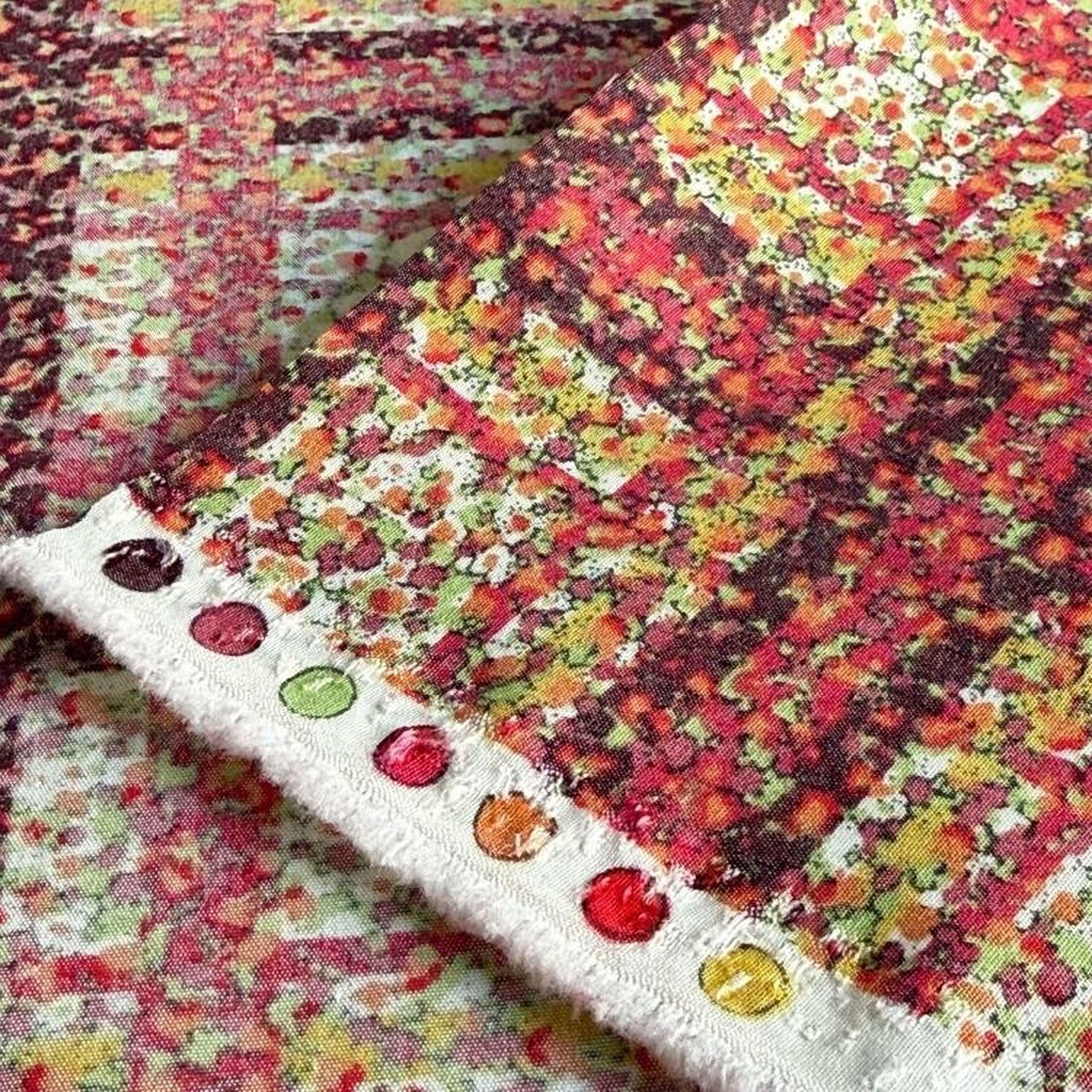 a close-up view of a fabric with a vibrant, colorful print featuring a repeating pattern of red, orange, yellow, and green hues. The fabric appears to be a piece of clothing or textile, with a white fringe or edge visible on the left side.