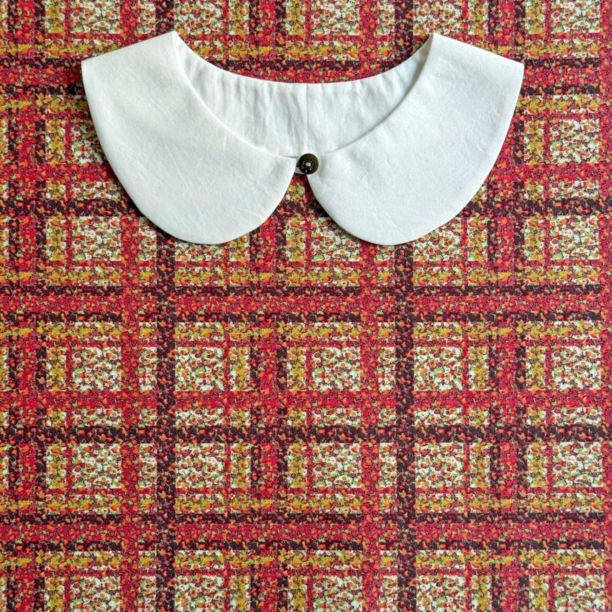 a white collar with a button, displayed against a background with a colorful, checkered pattern.