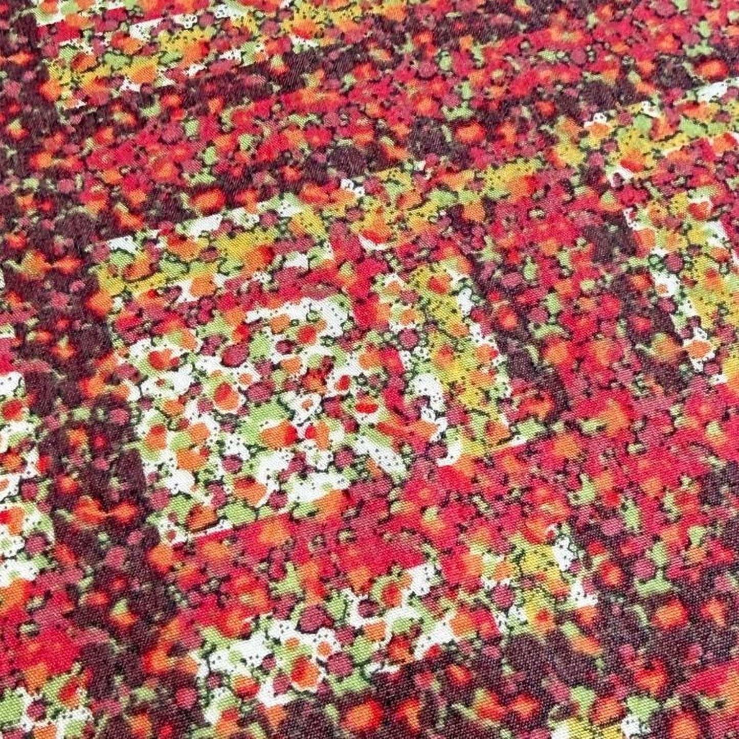 The image is a close-up of a fabric with a vibrant, abstract pattern of red, yellow, and green colors. The pattern appears to be a mix of different shapes and textures, creating a visually striking and dynamic design.
