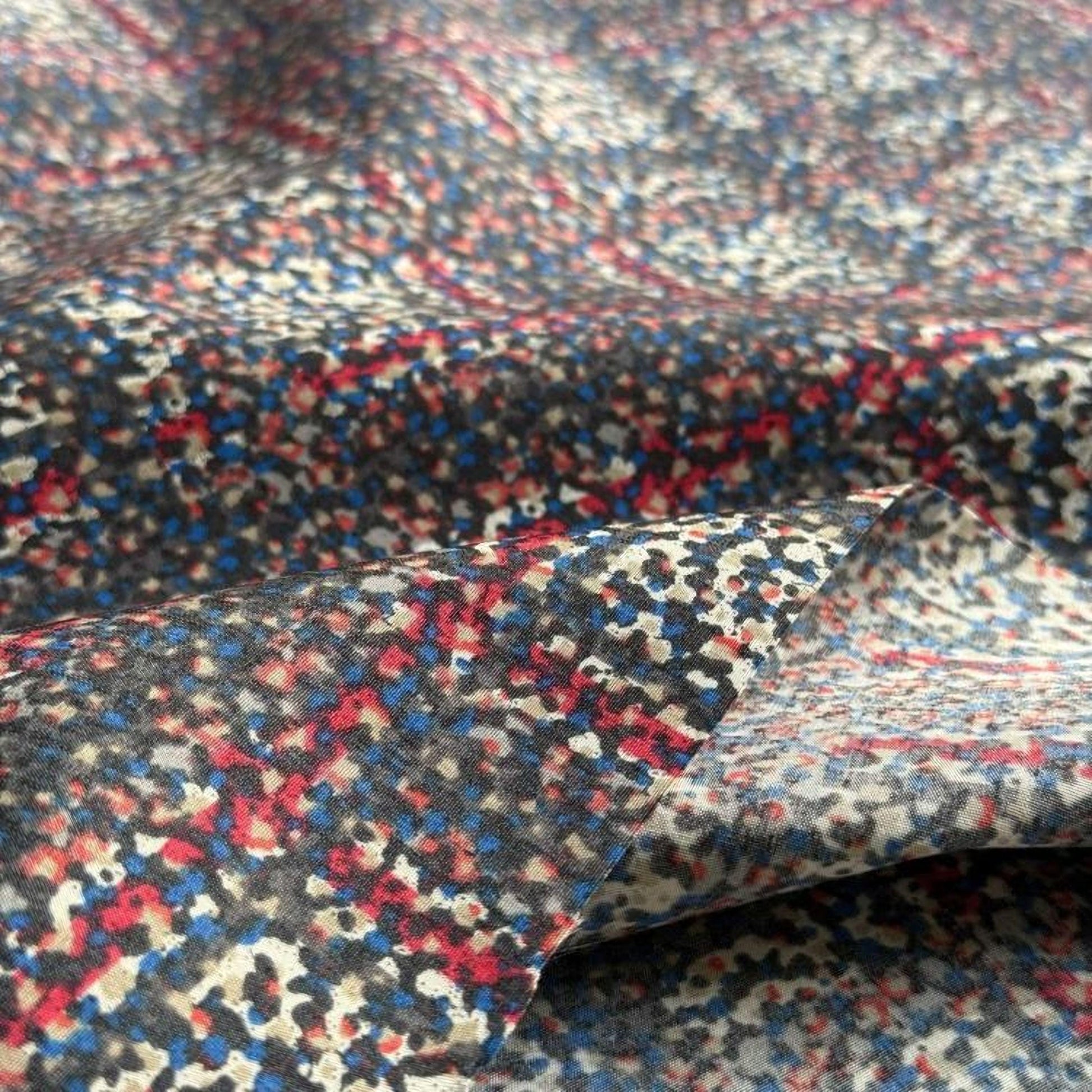 a close-up view of a fabric with a colorful, abstract pattern of red, blue, and gray dots or shapes.