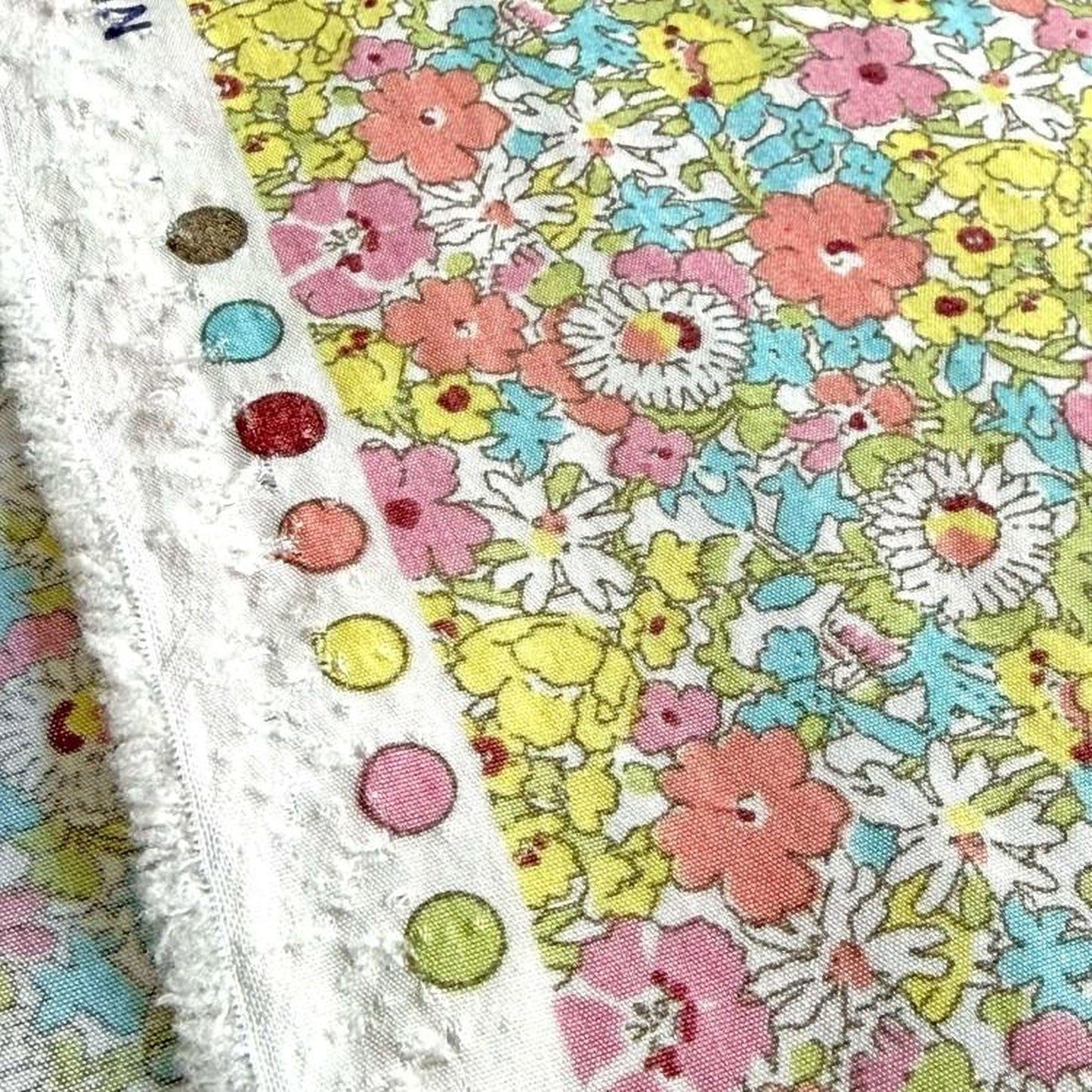a close-up view of a fabric with a vibrant floral pattern. The fabric is adorned with a variety of colorful flowers, including pink, yellow, and white blooms, creating a visually striking and lively design. The fabric appears to be a close-up of a piece of clothing or textile, with the intricate details of the flowers and the fabric's texture clearly visible.