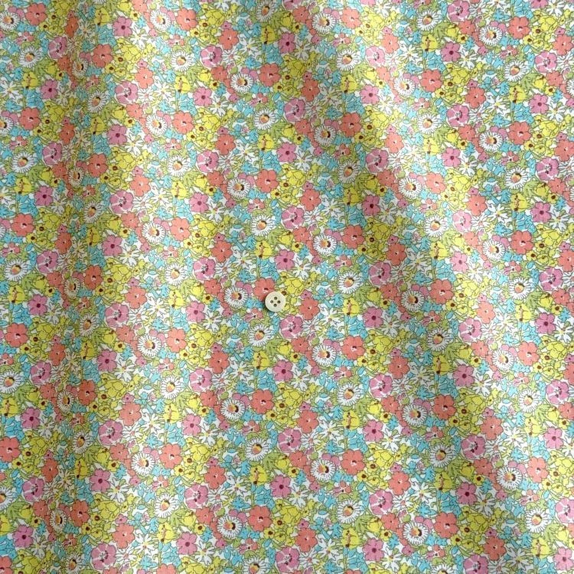 a close-up view of a fabric with a vibrant floral pattern in shades of yellow, pink, and blue. The pattern is composed of numerous small flowers, each with a unique color and shape, creating a visually striking and intricate design.