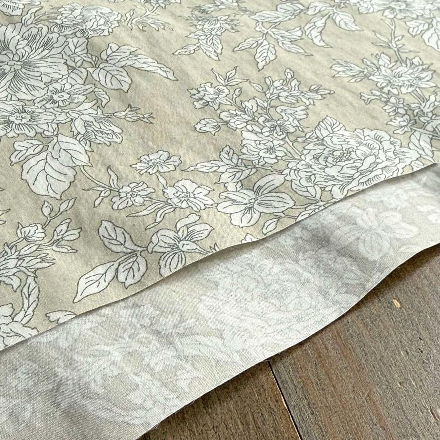 a close-up view of a fabric with a floral pattern, featuring white flowers and leaves on a beige background.