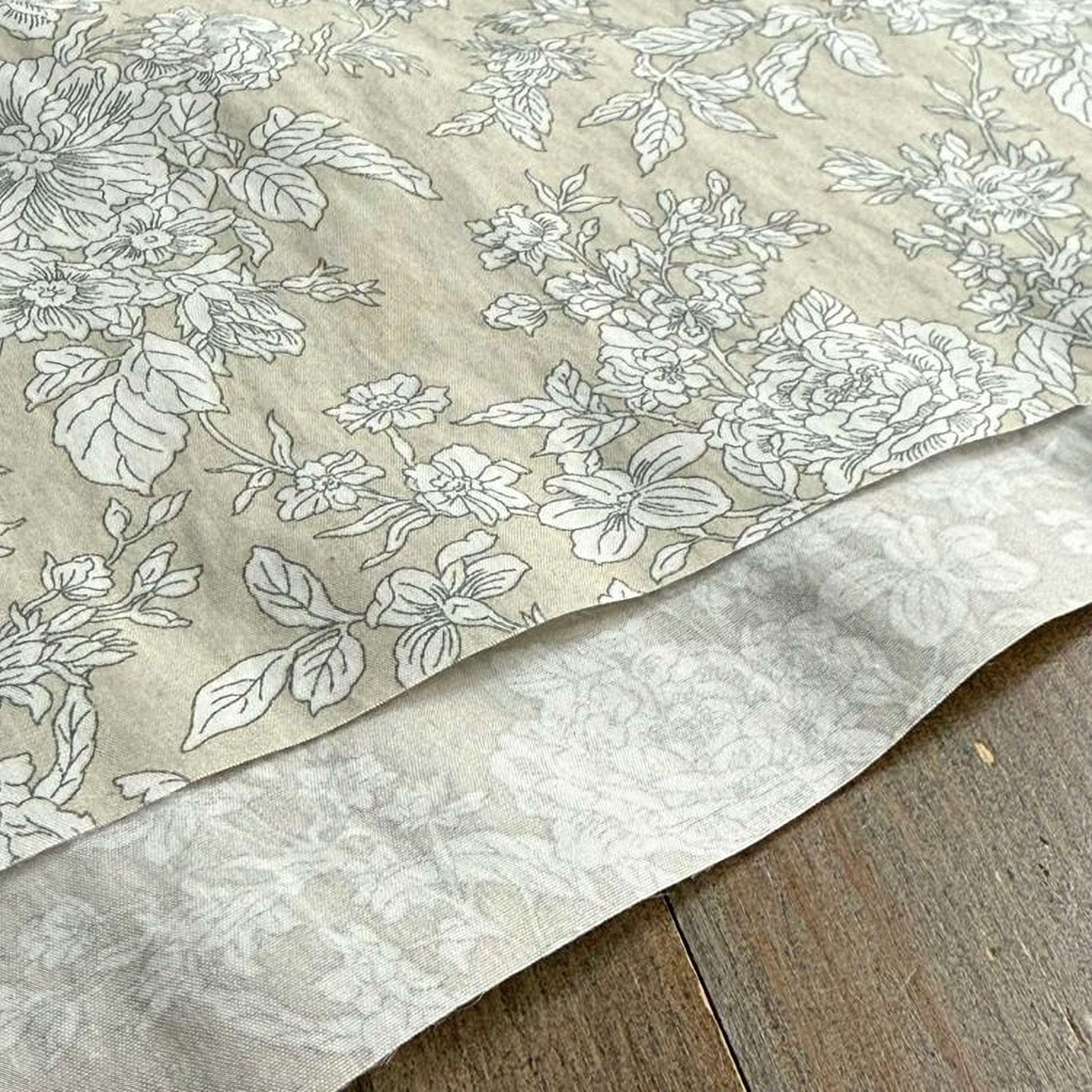 a close-up view of a fabric with a floral pattern, featuring white flowers and leaves on a beige background.