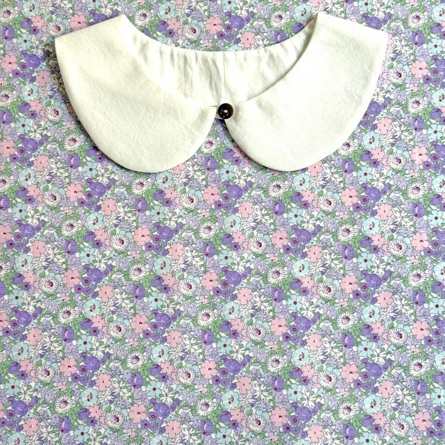 a white collar with a button, set against a background of a floral print in shades of purple and pink.