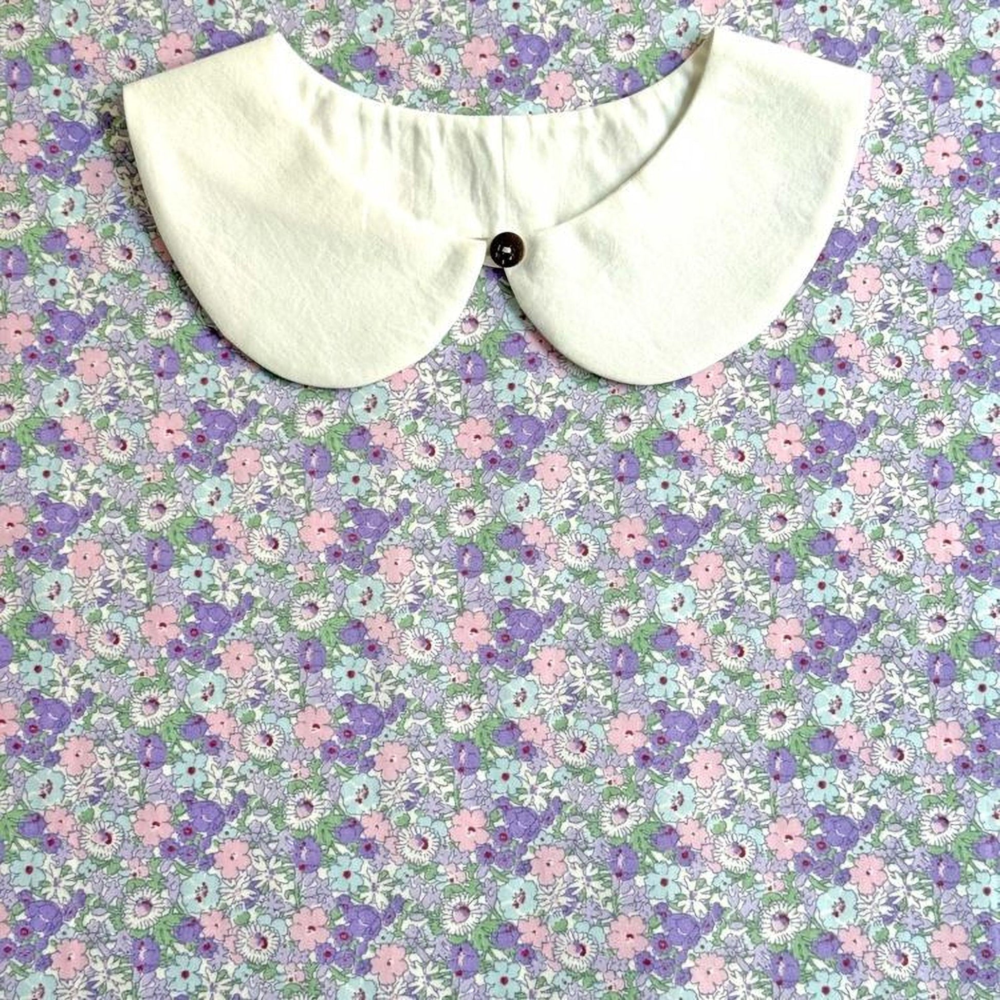 a white collar with a button, set against a background of a floral print in shades of purple and pink.