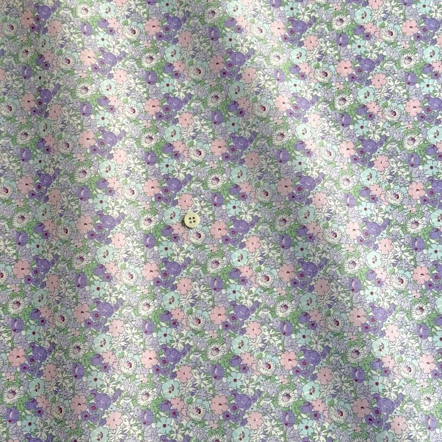 a fabric with a repeating pattern of purple and green flowers, with a small white button visible in the center.