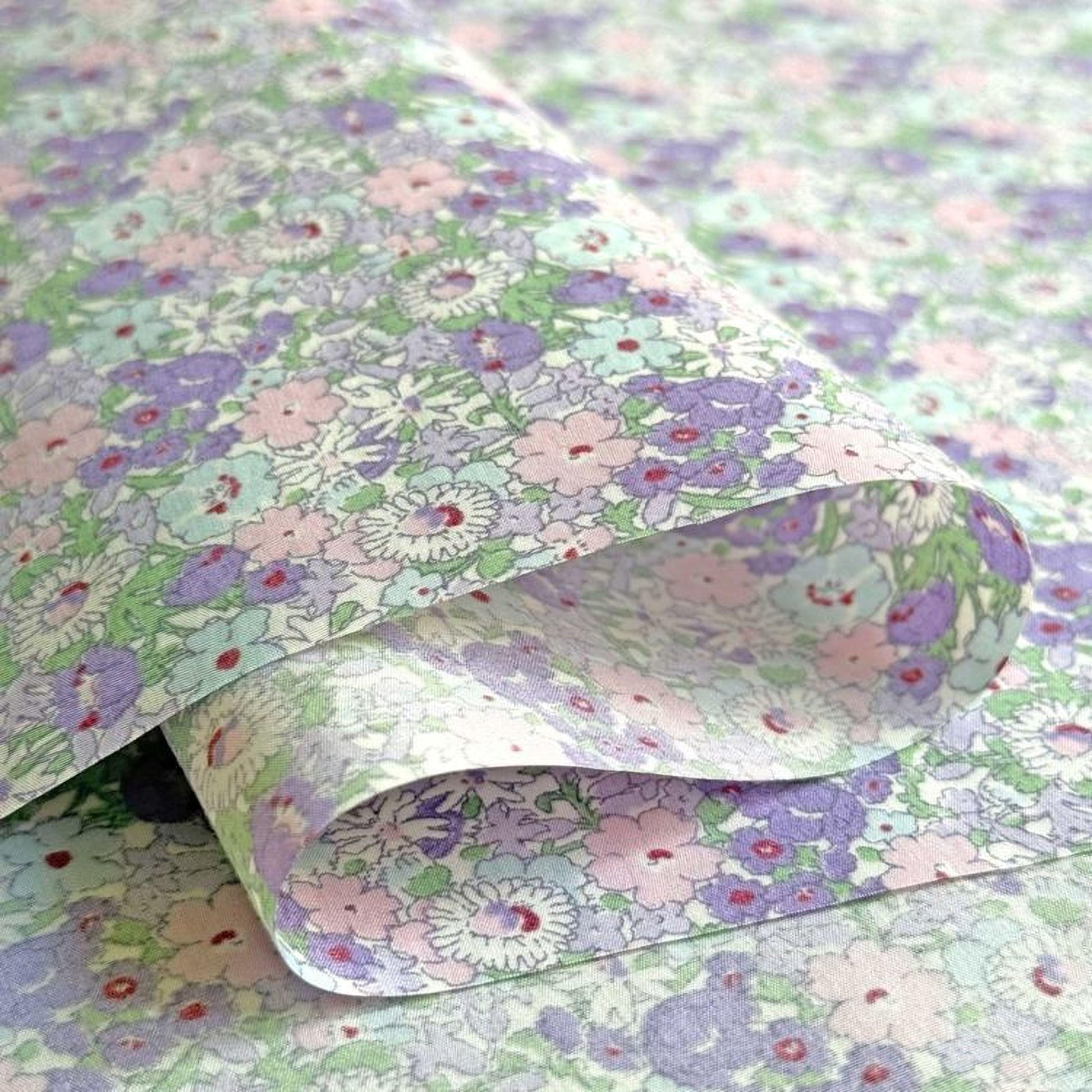 a close-up view of a fabric with a floral pattern in shades of purple and green. The fabric appears to be folded or rolled, revealing the intricate design of the flowers.