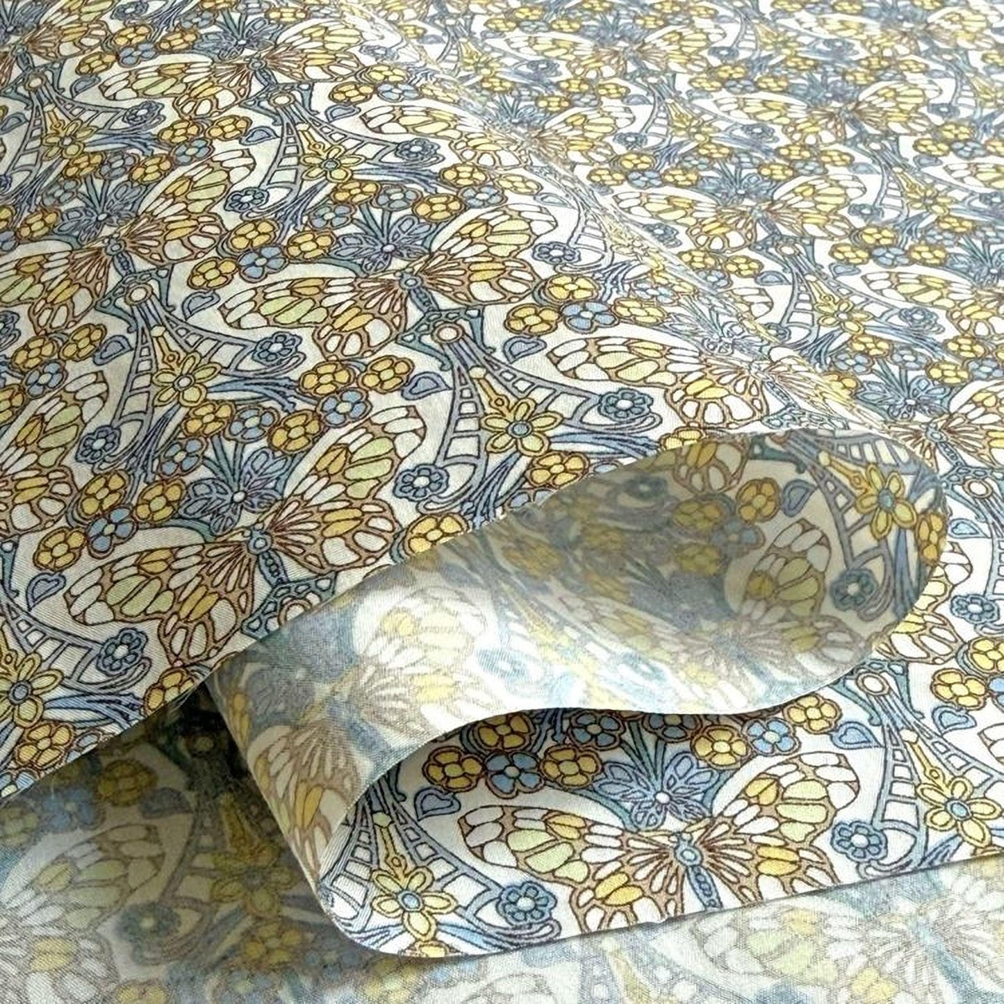 a close-up view of a fabric with a repeating pattern of yellow and blue flowers and leaves. The pattern is intricate and detailed, creating a visually appealing design.