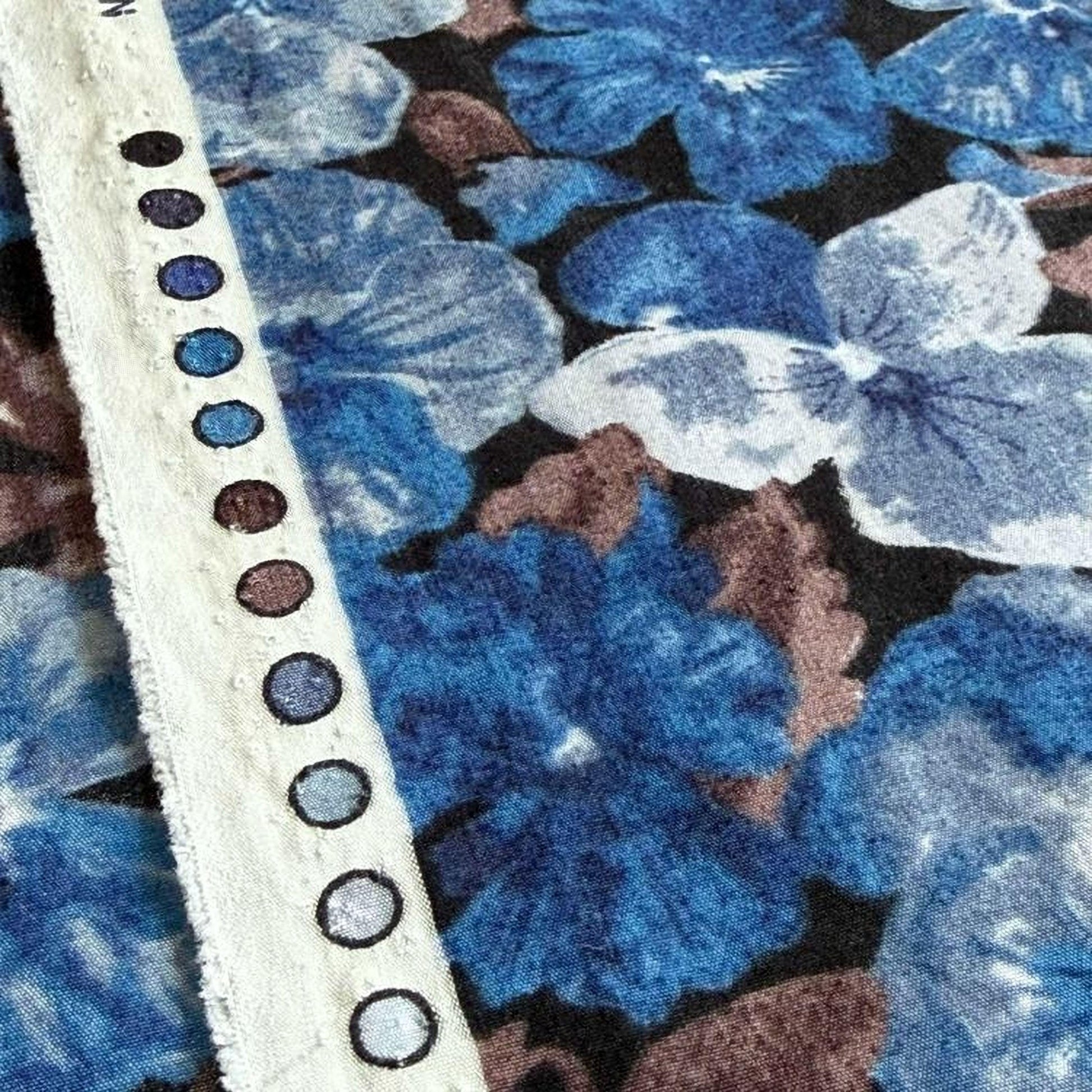 a close-up view of a fabric with a floral pattern in shades of blue and brown. The fabric appears to be a piece of clothing or textile, with a white strap or belt visible on the left side of the frame.