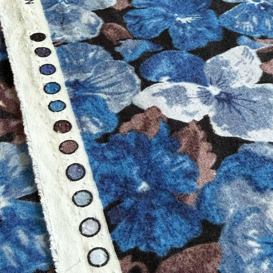 a close-up view of a fabric with a floral pattern in shades of blue and brown. The fabric appears to be a piece of clothing or textile, with a white strap or belt visible on the left side of the frame.