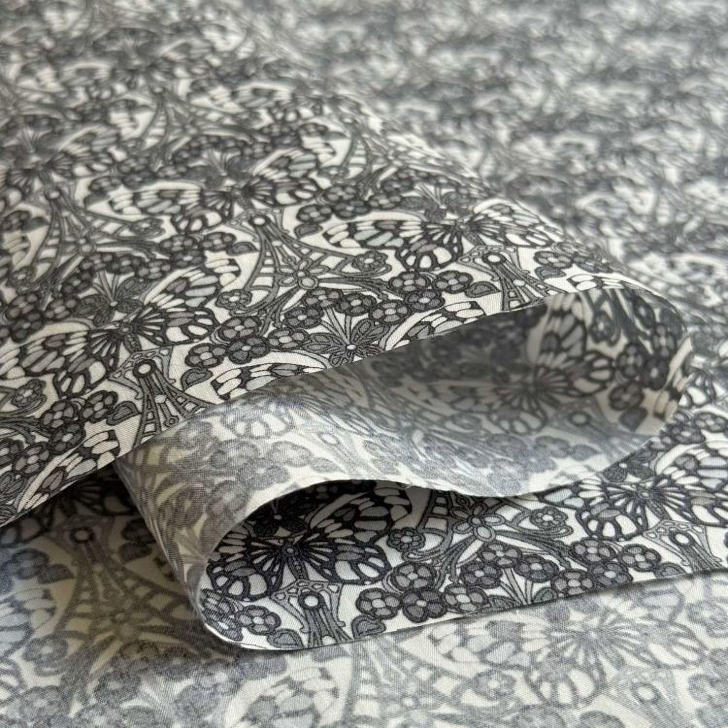 a close-up view of a fabric with a repeating pattern of black and white flowers or butterflies. The pattern is intricate and detailed, creating a visually striking and textured surface.