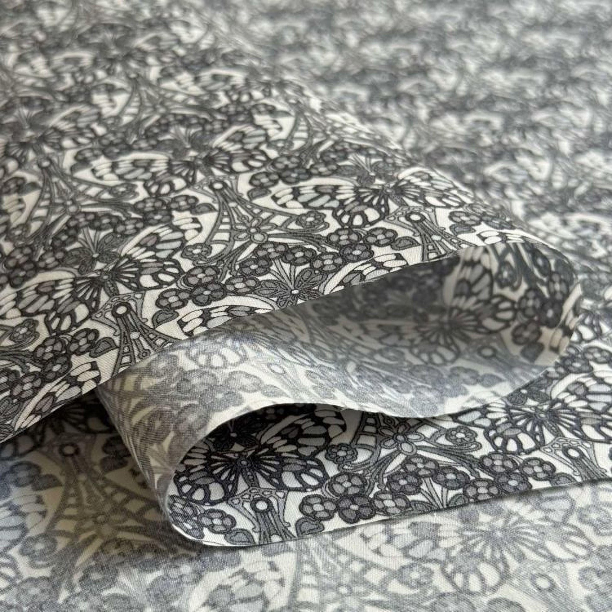 a close-up view of a fabric with a repeating pattern of black and white flowers or butterflies. The pattern is intricate and detailed, creating a visually striking and textured surface.