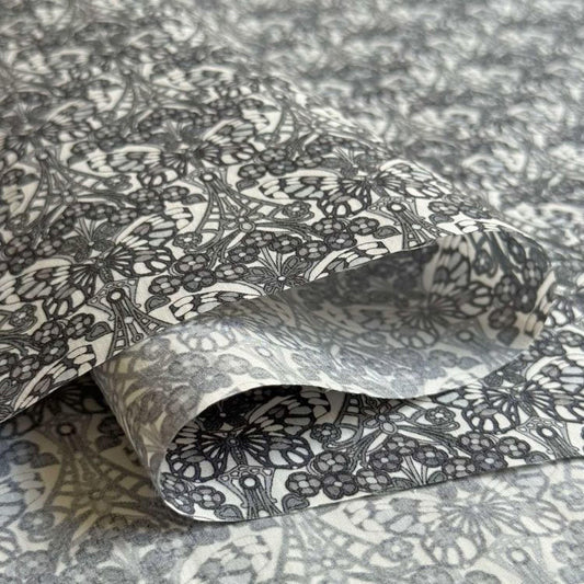 a close-up view of a fabric with a repeating pattern of black and white flowers or butterflies. The pattern is intricate and detailed, creating a visually striking and textured surface.